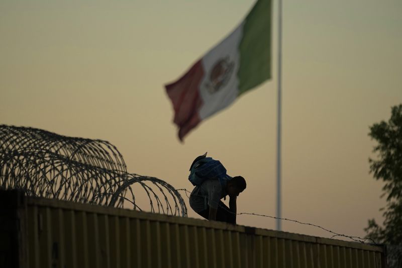 A migrant who crossed the Rio Grande from Mexico to the U.S. works their way through and over concertina wire and box car barriers, Sept. 22, in Eagle Pass, Texas.