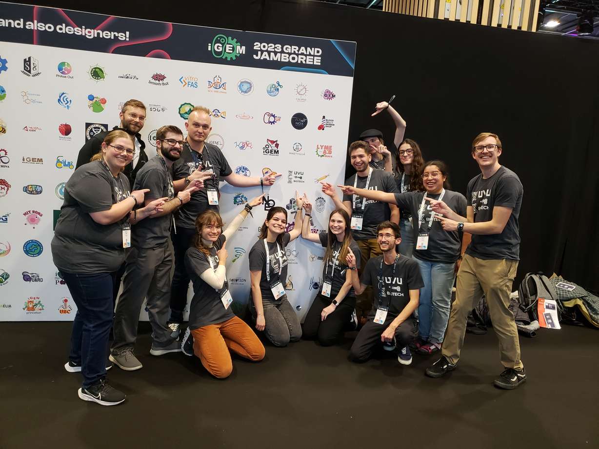 A team of UVU students point to their university's logo on a poster at the International Genetically Engineered Machine Jamboree competition in Paris. The team won a silver medal for its genetically modified algae that could act as a sponge to soak up toxins and prevent harmful algal blooms in the Utah Lake.