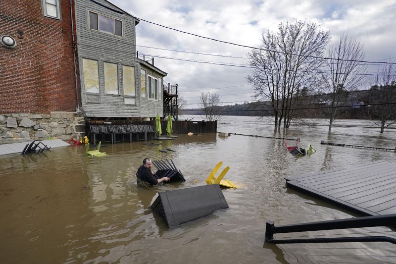 Nathan Sennett wades to retrieve furniture in hip-deep water on the patio of the Quarry Tap Room, Tuesday, in Hallowell, Maine. Waters continue to rise in the Kennebec River following Monday's severe storm.