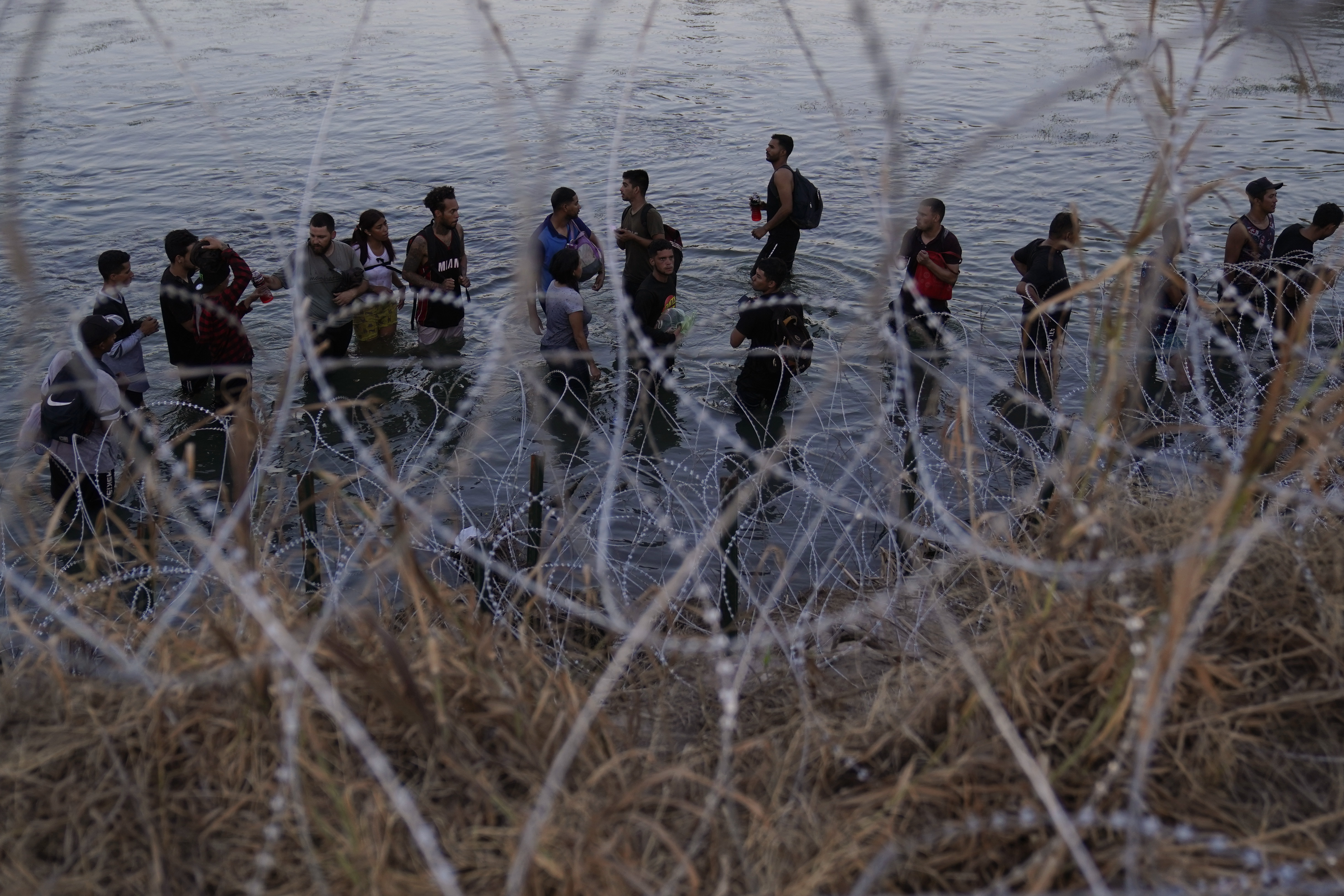 Migrants wait to climb over concertina wire after they crossed the Rio Grande and entered the U.S. from Mexico, Sept. 23, in Eagle Pass, Texas. The White House and Mexico's president are sharply criticizing a new Texas law allowing police to arrest migrants who illegally cross into the U.S.