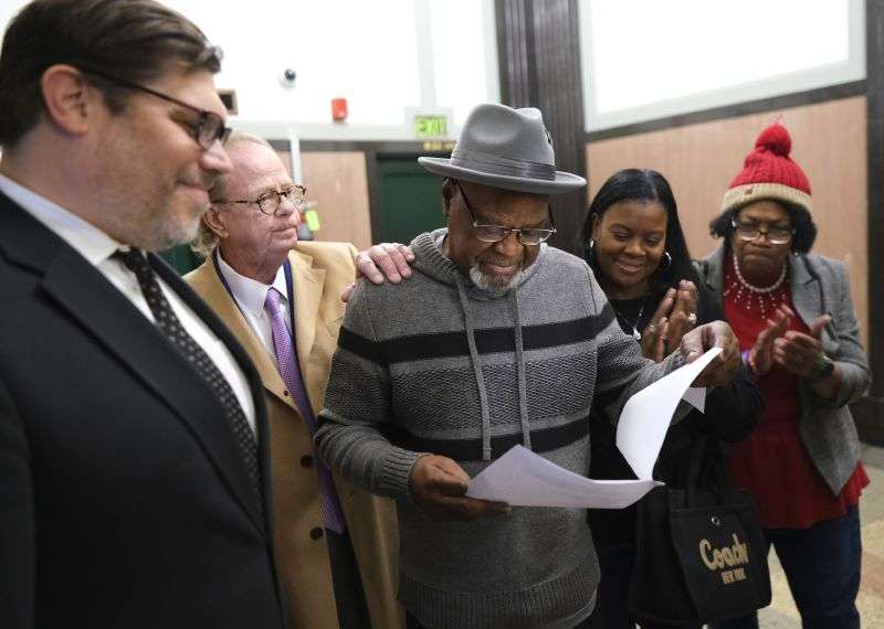 Glynn Simmons reads the court order as his attorneys Joe Norwood and John Coyle, left, and his niece Cecilia Hawthorne and Madeline Jones, right, look on after after Judge Amy Palumbo ruled to approve Simmons' "actual innocence" claim during a hearing at the Oklahoma County Courthouse Tuesday in Oklahoma City, Okla.