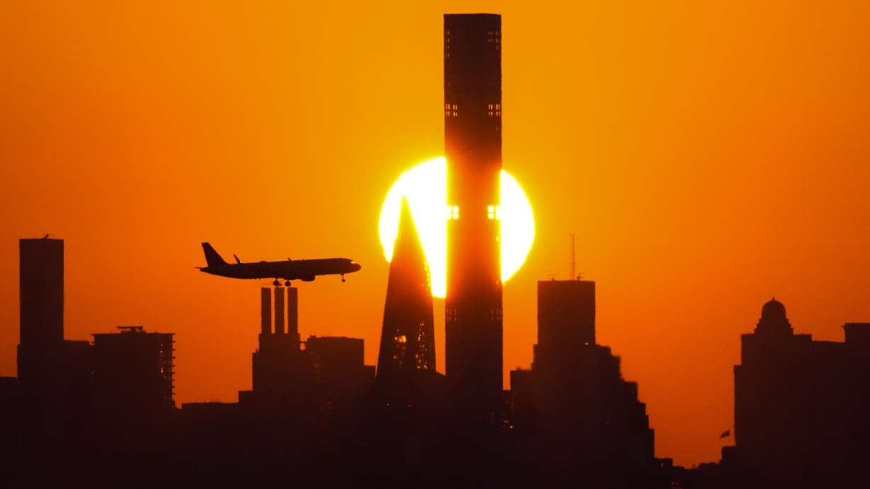 The sun sets behind the Manhattan skyline as plane approaches LaGuardia Airport in New York. Holiday travel is kicking off on highways, trains and airports this week.