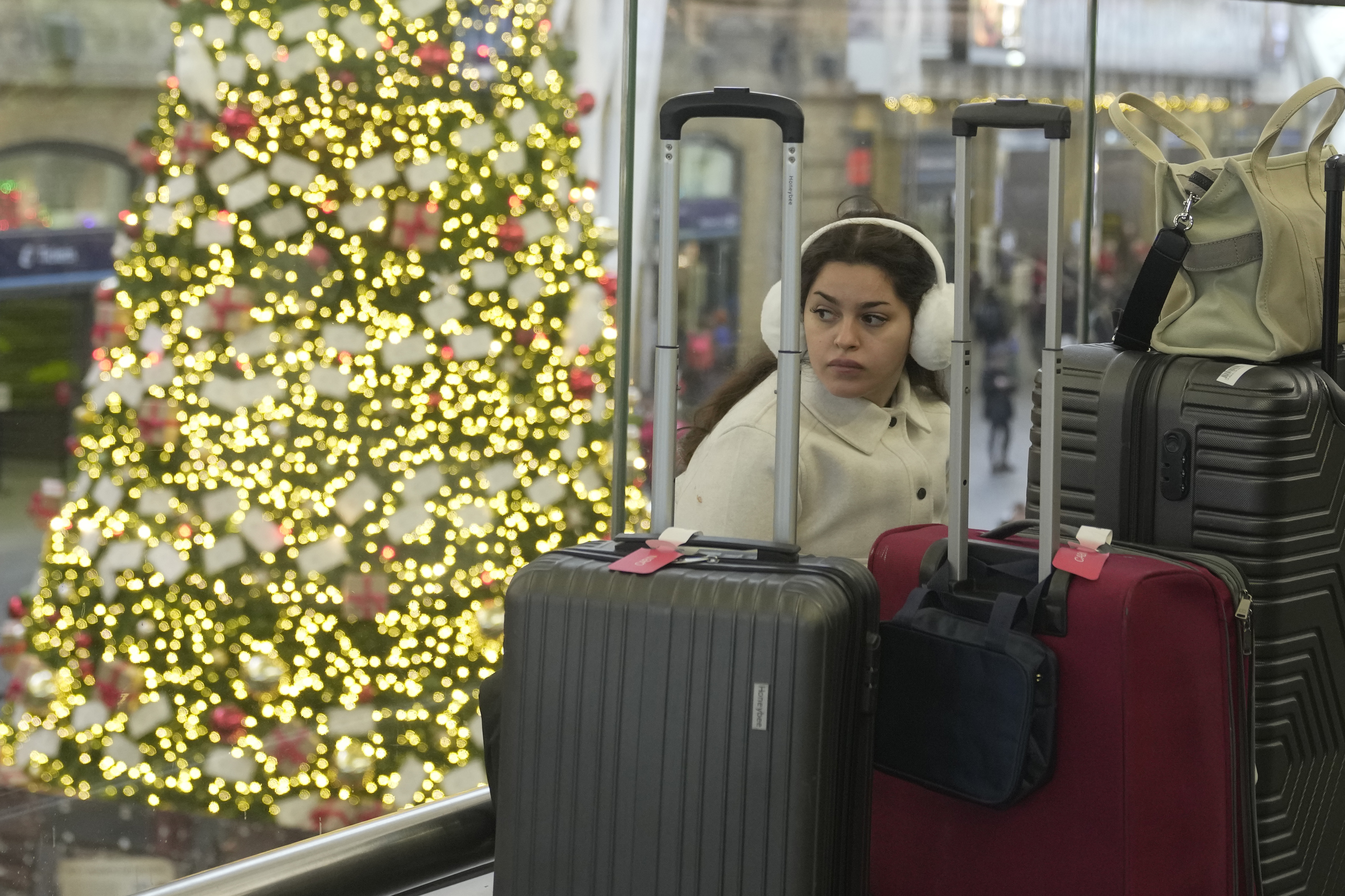 A traveller waits for a train near a large Christmas tree at King's Cross Station in London, Thursday. Rail travelers over the Christmas holiday season will have to contend with disruptions to services due to engineering work and bad weather.