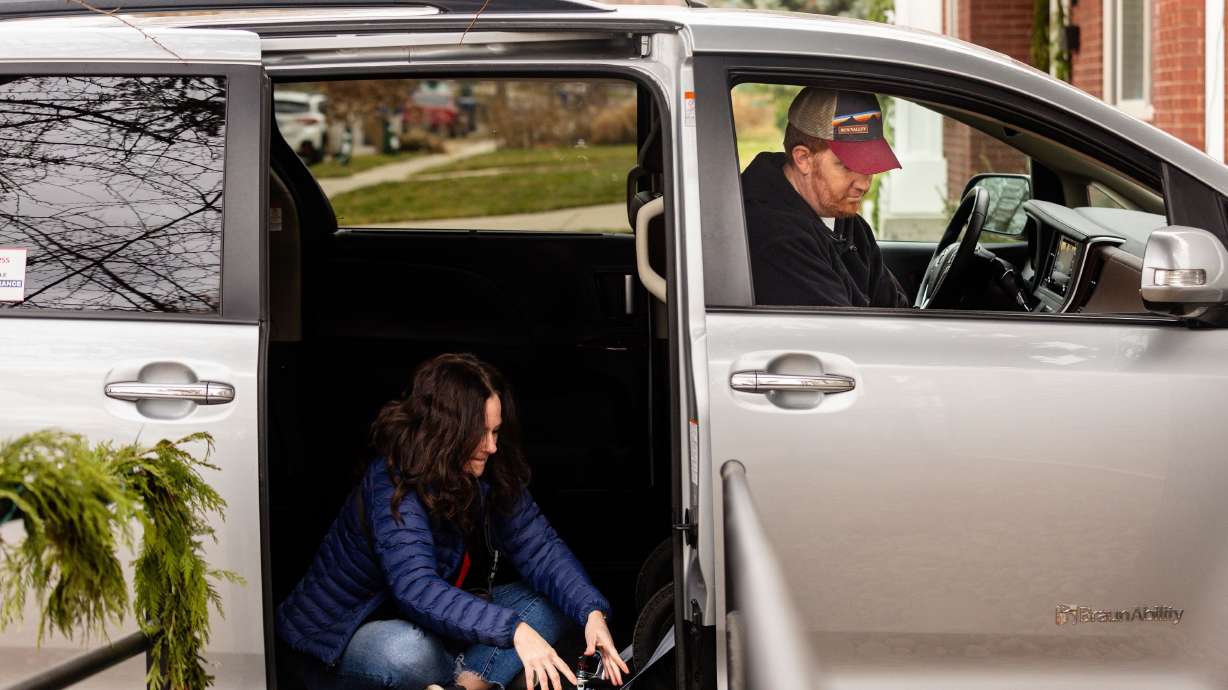Whitney Cunningham buckles Sean Cunningham’s wheelchair as they prepare to leave for a doctor’s appointment outside their home in Salt Lake City on Wednesday.