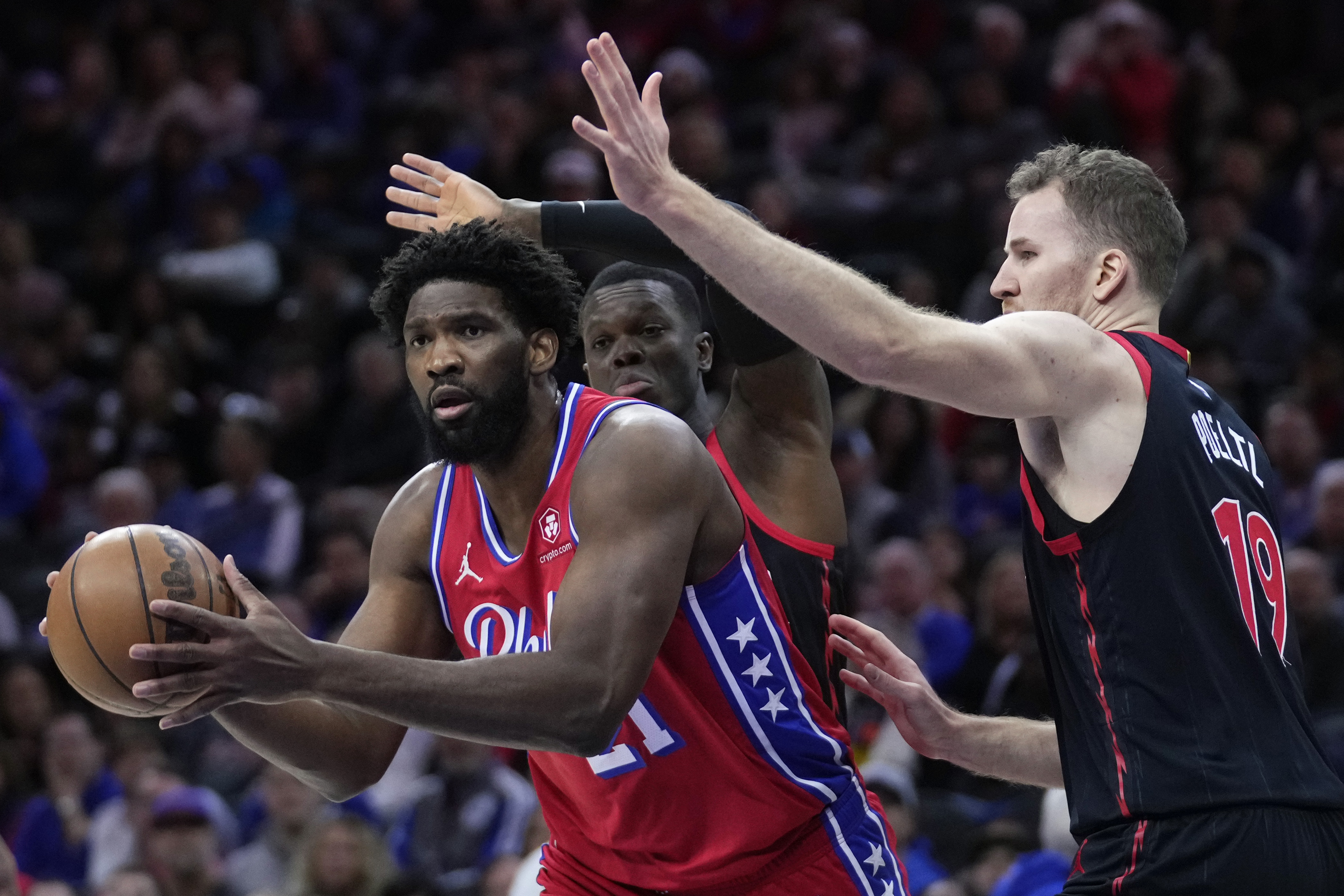 Philadelphia 76ers' Joel Embiid, left, tries to get by Toronto Raptors' Dennis Schroder, center, and Jakob Poeltl during the first half of an NBA basketball game, Friday, Dec. 22, 2023, in Philadelphia. 