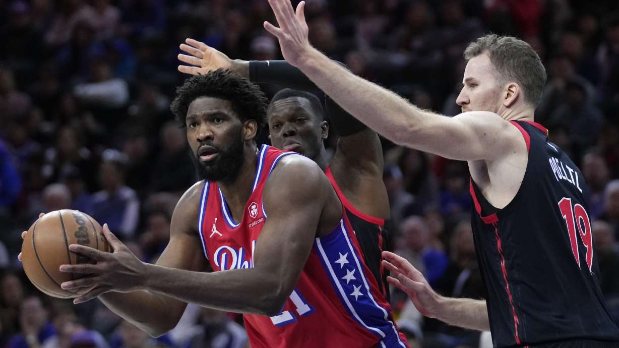 Philadelphia 76ers' Joel Embiid, left, tries to get by Toronto Raptors' Dennis Schroder, center, and Jakob Poeltl during the first half of an NBA basketball game, Friday, Dec. 22, 2023, in Philadelphia.