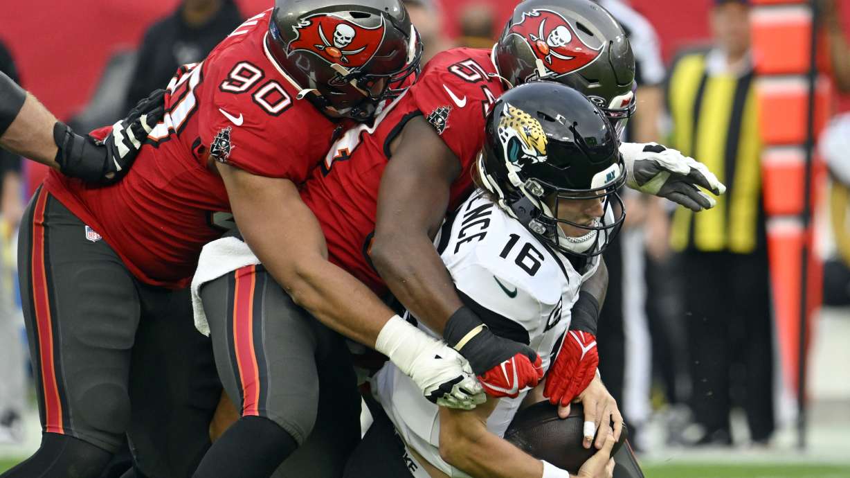 Tampa Bay Buccaneers defensive end Logan Hall (90) and linebacker Lavonte David, center, sack Jacksonville Jaguars quarterback Trevor Lawrence (16) during the first half of an NFL football game Sunday, Dec. 24, 2023, in Tampa, Fla.
