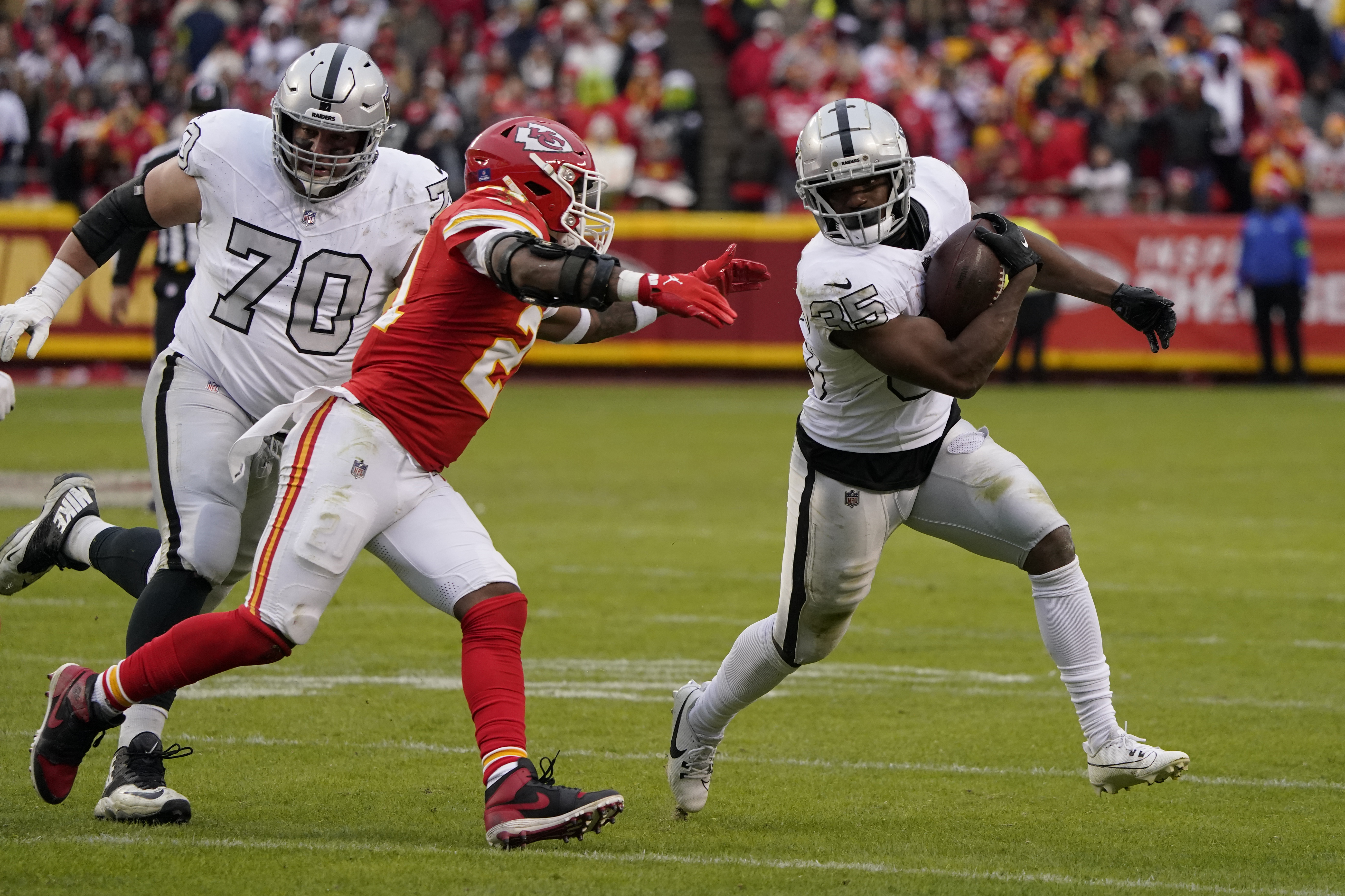Las Vegas Raiders running back Zamir White (35) runs with the ball as Kansas City Chiefs safety Mike Edwards defends and Raiders guard Greg Van Roten looks on during the second half of an NFL football game Monday, Dec. 25, 2023, in Kansas City, Mo.
