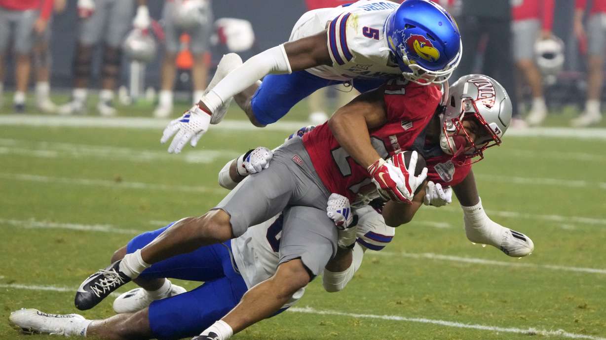 UNLV wide receiver Jacob De Jesus is tackled by Kansas safety O.J. Burroughs (5) and linebacker Taiwan Berryhill Jr. during the first half of the Guaranteed Rate Bowl NCAA college football game Tuesday, Dec. 26, 2023, in Phoenix.