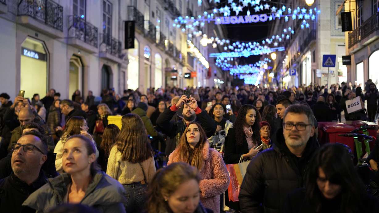 People look up at Christmas lights as crowds stroll around downtown Lisbon's Chiado neighborhood, Saturday evening, Dec. 23. The world population grew by 75 million people over the past year and on New Year's Day it will stand at more than 8 billion people.