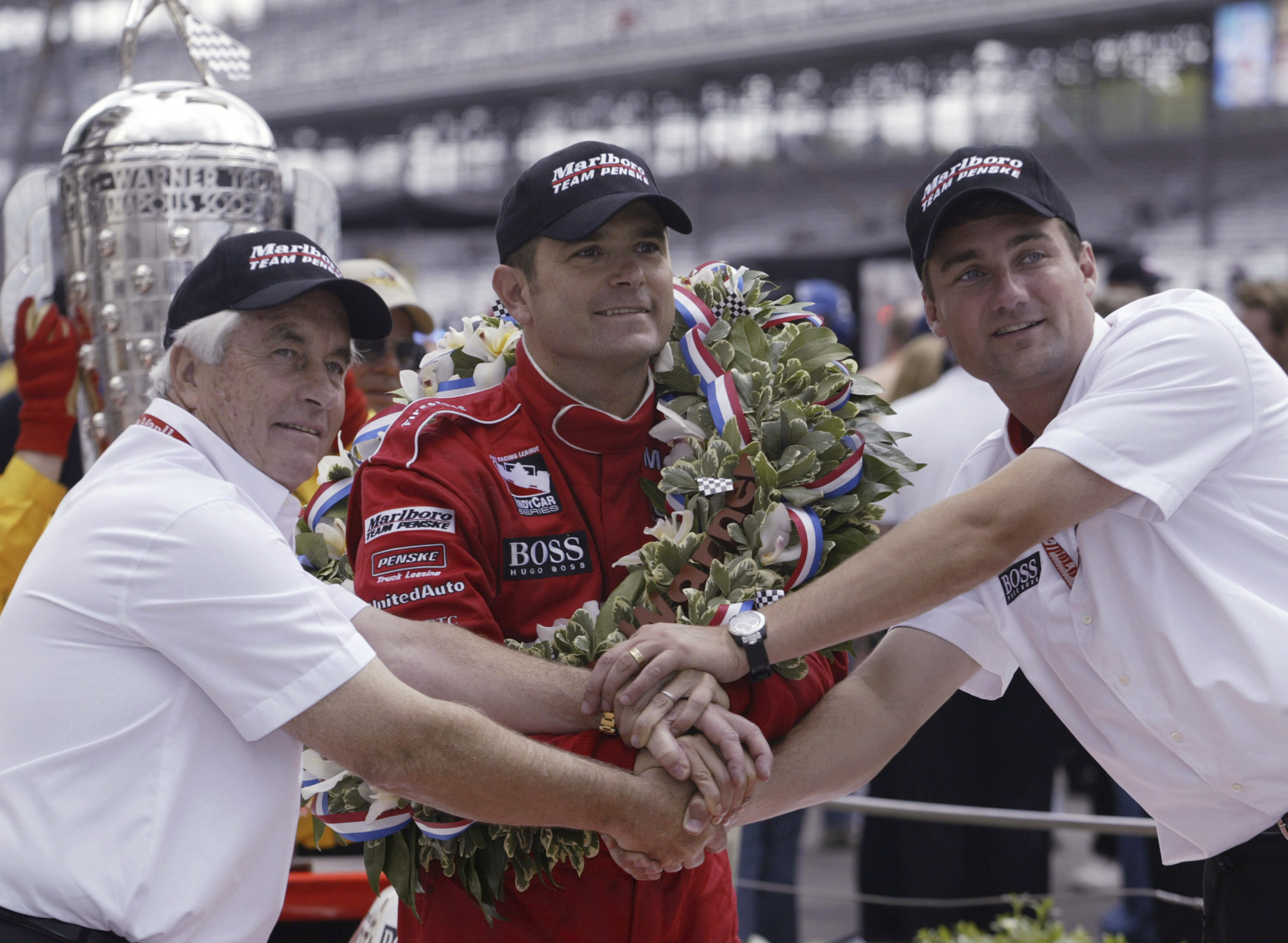 FILE - Car owner Roger Penske, left, and Tim Cindric, right, president of Penske Racing, clasp hands with Indianapolis 500 winner Gil de Ferran, of Brazil, on May 25, 2003, in Indianapolis. De Ferran, winner of the 2003 Indy 500 and holder of the closed-course land speed record, died Friday, Dec. 29, 2023, while racing with his son at The Concourse Club in Florida, multiple former colleagues confirmed to The Associated Press. He was 56. 