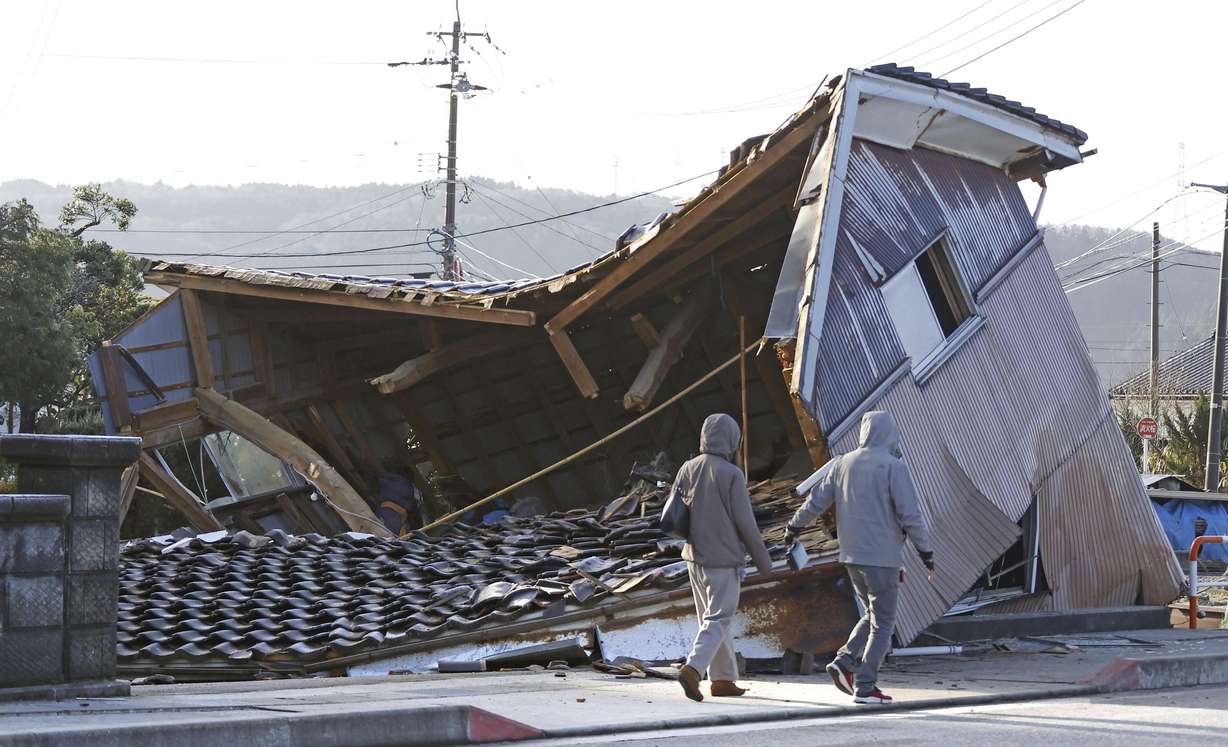 People walk by a building collapsed following an earthquake in Shikamachi, Ishikawa prefecture, Japan Tuesday.