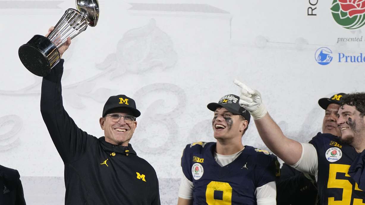 Michigan head coach Jim Harbaugh holds the winner's trophy next to quarterback J.J. McCarthy (9) after a win over Alabama in the Rose Bowl CFP NCAA semifinal college football game Monday, Jan. 1, 2024, in Pasadena, Calif.