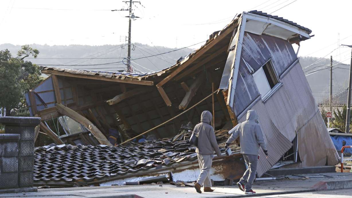 People walk by a building collapsed following an earthquake in Shikamachi, Ishikawa prefecture, Japan Tuesday. A series of powerful earthquakes has hit western Japan, leaving at least 57 people dead and damaging thousands of buildings, vehicles and boats.
