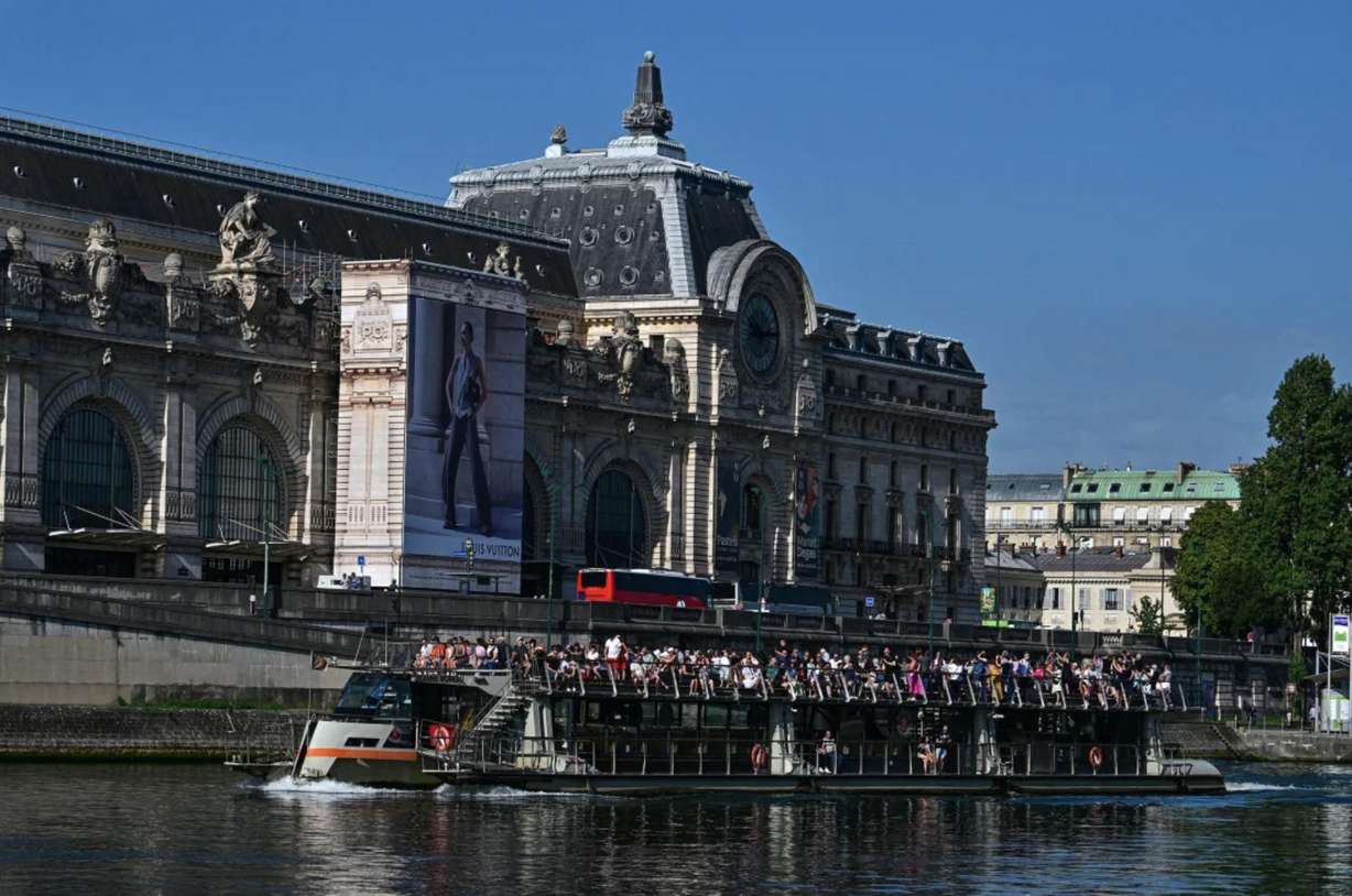 Tourists tour Paris aboard an open excursion boat on the Seine, with the Musee d'Orsay in the background, on August 22.