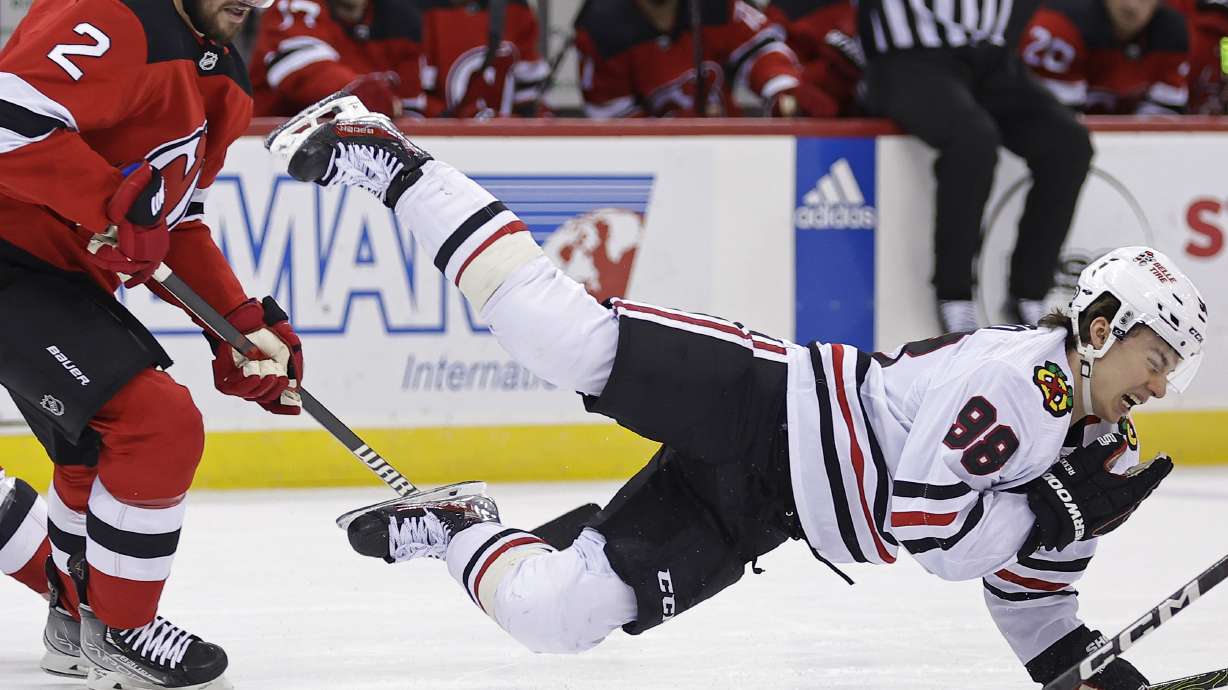Chicago Blackhawks center Connor Bedard falls to the ice after being checked by New Jersey Devils defenseman Brendan Smith (2) during the first period of an NHL hockey game Friday, Jan. 5, 2024, in Newark, N.J.