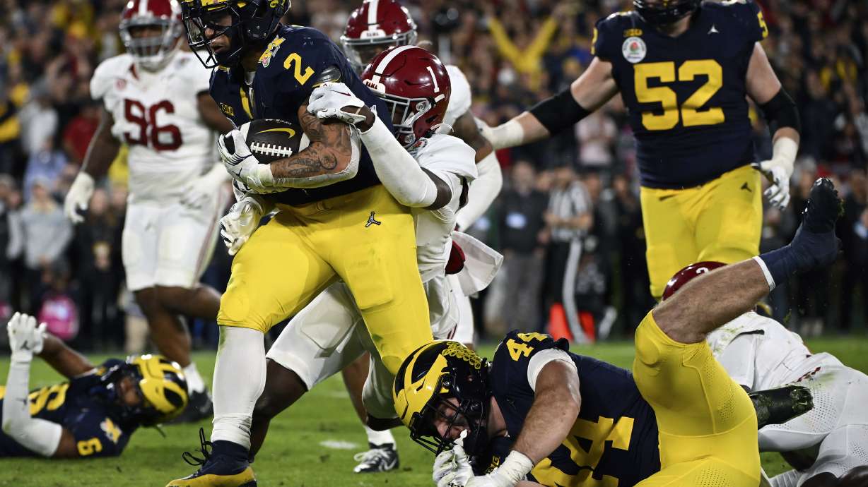 FILE - Michigan running back Blake Corum (2) runs in for a touchdown past Alabama defensive back Kool-Aid McKinstry (1) during overtime at the Rose Bowl CFP NCAA semifinal college football game Jan. 1, 2024, in Pasadena, Calif. Nonprofits Hail! Impact, which supports the University of Michigan's Wolverines, and Montlake Futures, which supports athletes at the University of Washington, are set to benefit regardless of who wins the national championship.