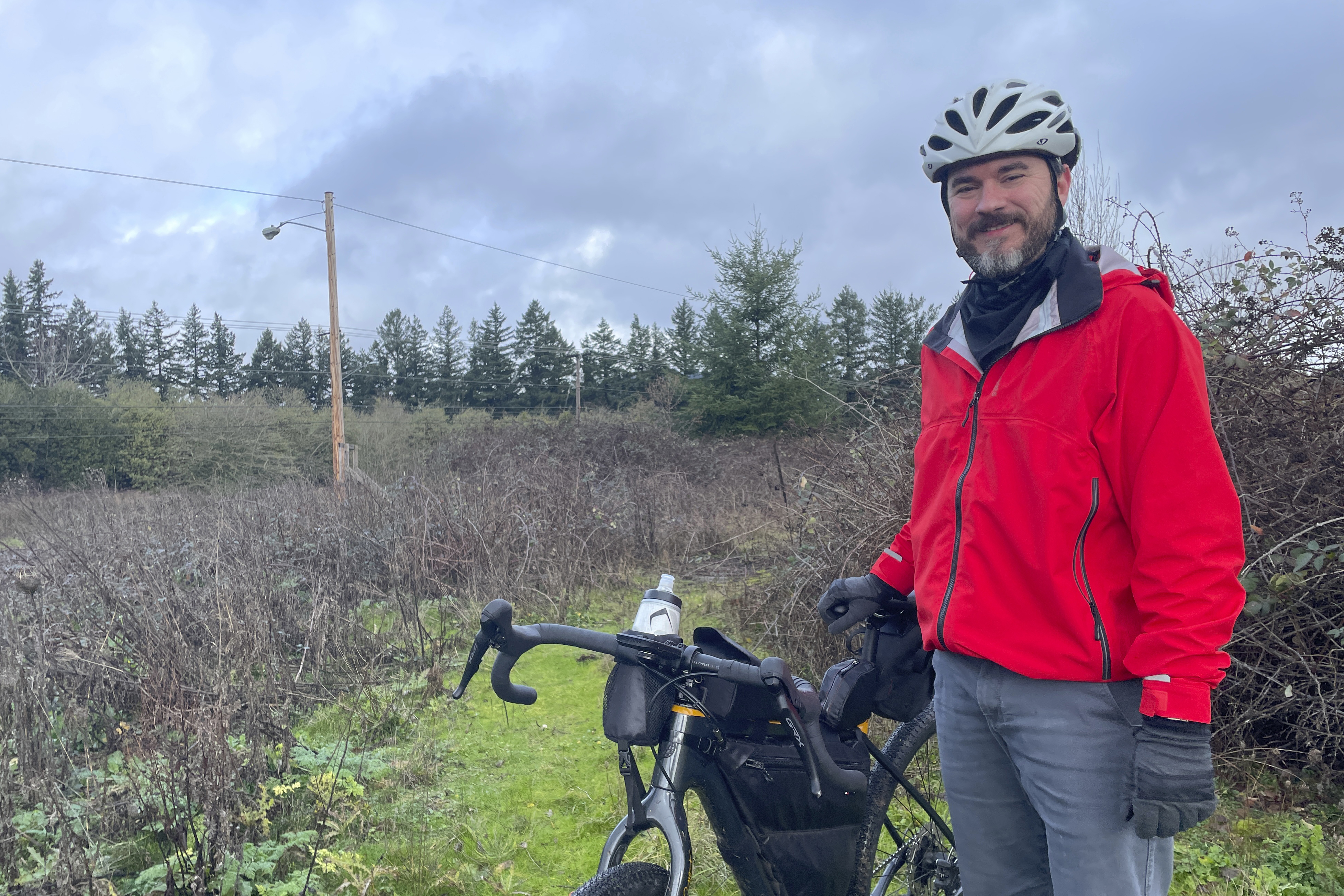 Adam Pirkle stands with his bicycle on the edge of a densely thicketed area in the Cedar Hills area of southwest Portland, Ore., Sunday. Pirkle said he rode 14 miles looking for the wreckage of the fuselage that detached from a Boeing 737 Max 9 shortly after the takeoff of an Alaska Airlines flight on Friday.