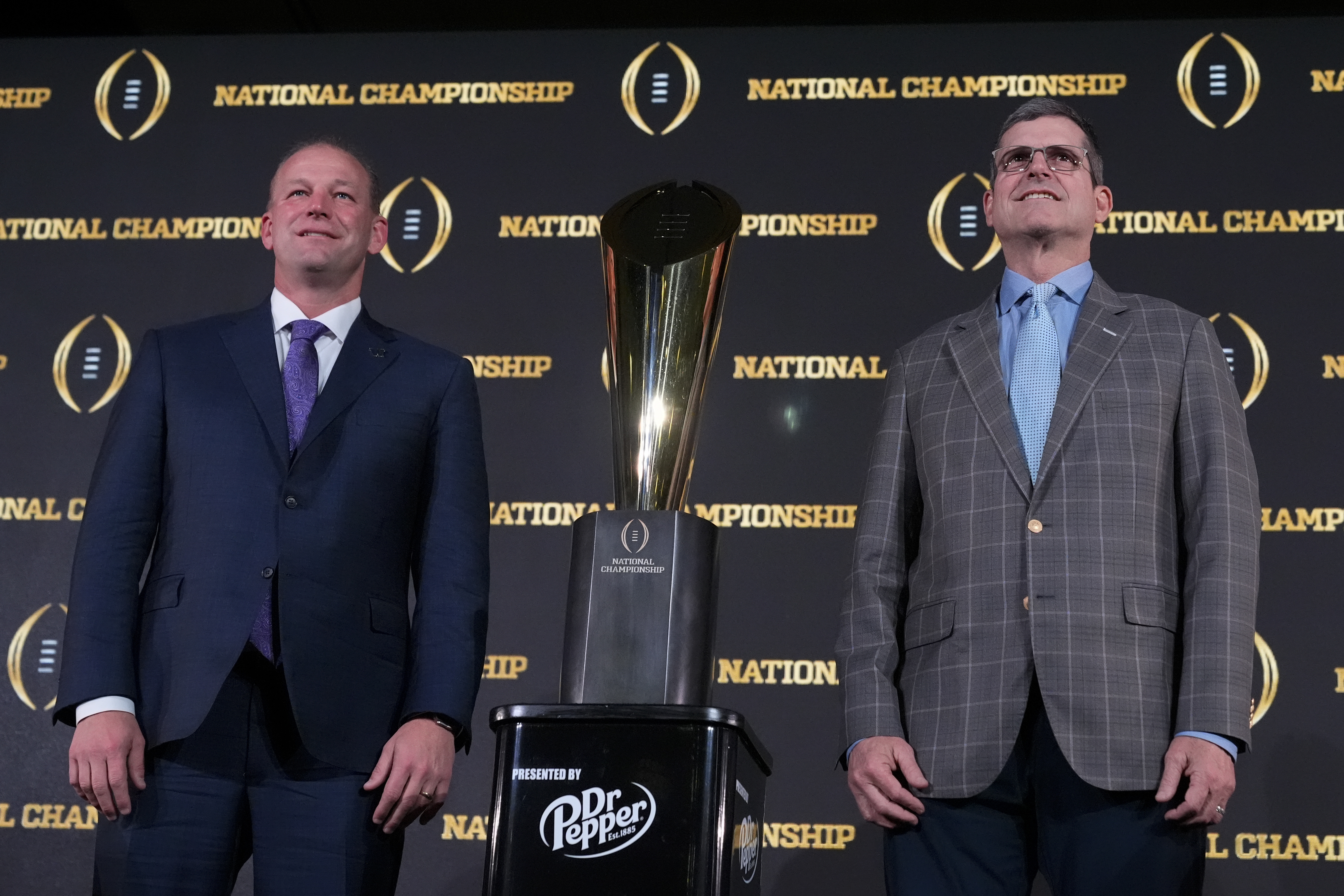 Washington head coach Kalen DeBoer, left, and Michigan head coach Jim Harbaugh pose with the trophy after a news conference ahead of the national championship NCAA College Football Playoff game between Washington and Michigan Sunday, Jan. 7, 2024, in Houston. The game will be played Monday.