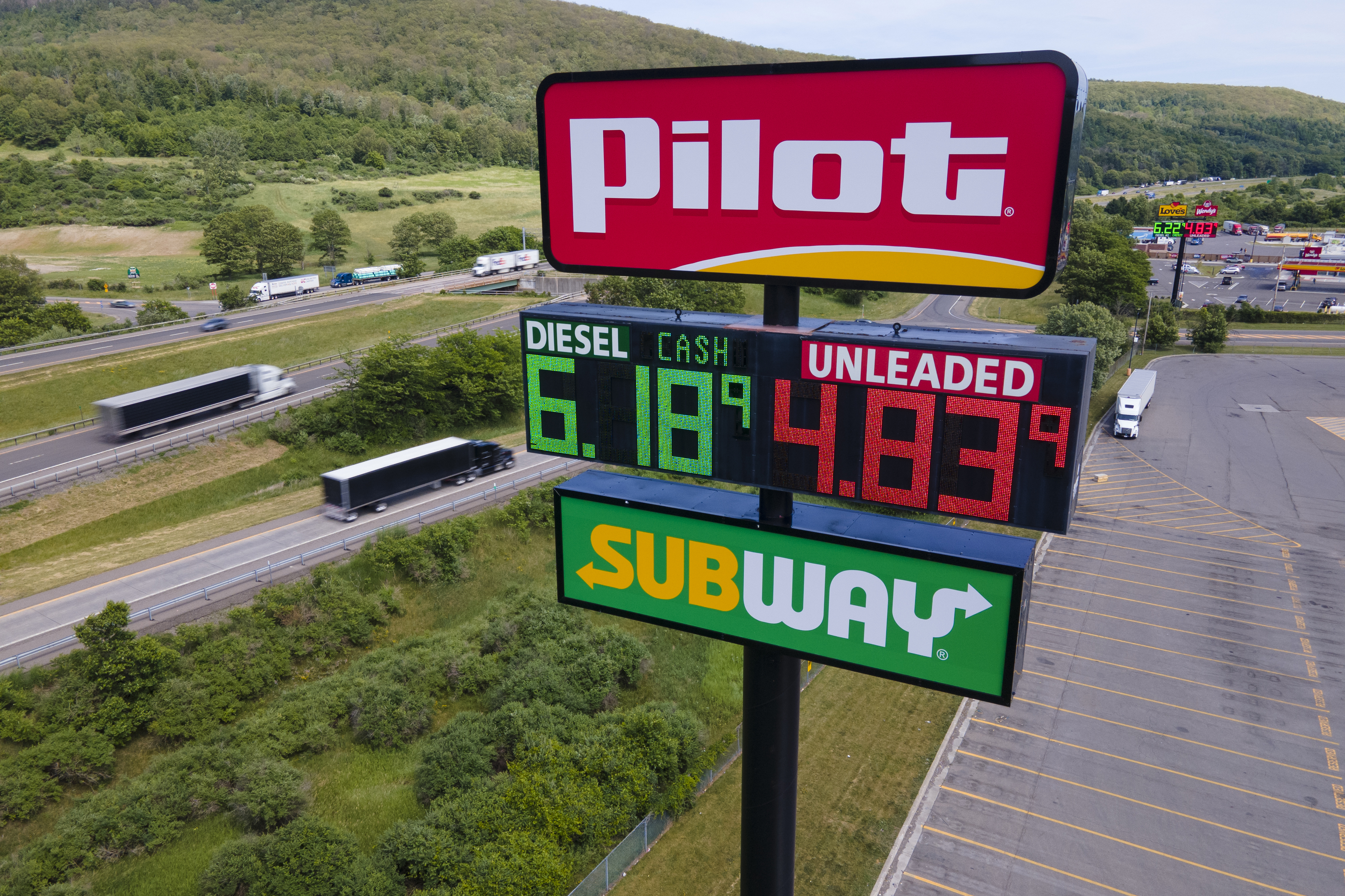 FILE - Trucks and cars drive by a Pilot Travel Center sign displaying fuel prices, June 20, 2022, in Bath, N.Y. The clock is ticking for Cleveland Browns owner Jimmy Haslam and his family to decide whether to sell their remaining stake in the Pilot truck stop chain to fellow billionaire Warren Buffet's Berkshire Hathaway company. A trial had been scheduled to start Monday, Jan. 8, 2023, in Delaware in a dispute over accounting practices at Pilot Travel Centers. 