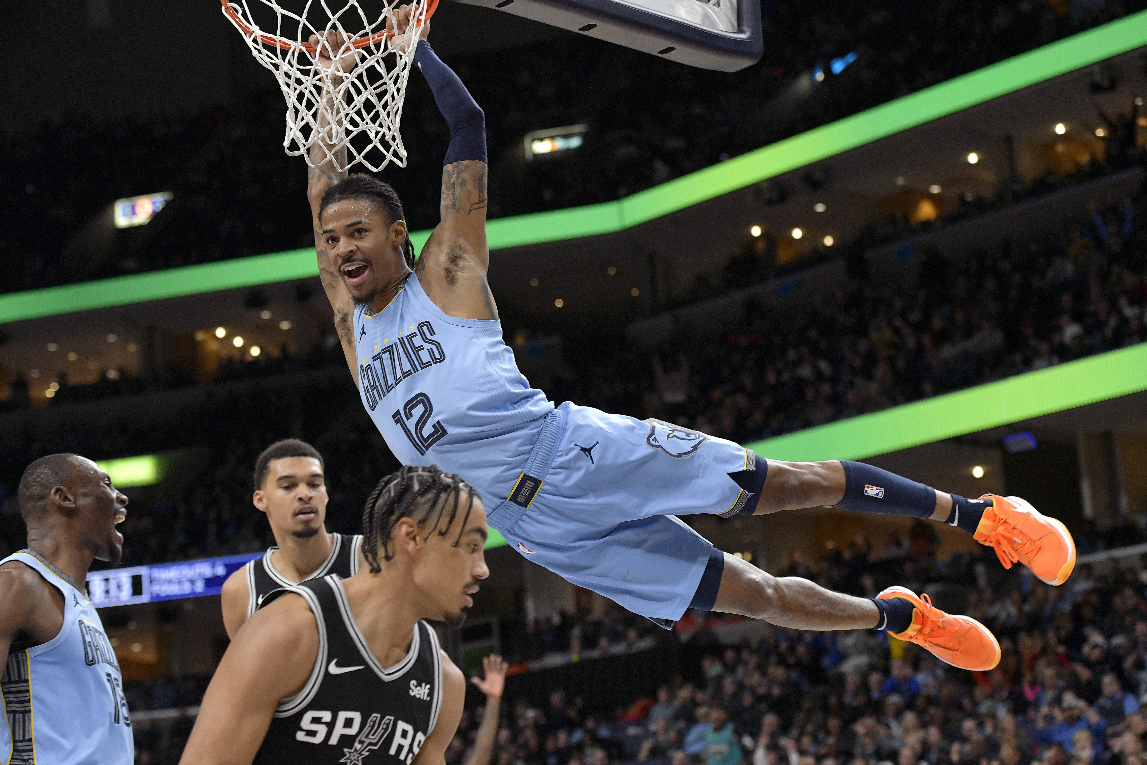 Memphis Grizzlies guard Ja Morant (12) hangs from the rim after dunking against the San Antonio Spurs in the second half of an NBA basketball game Tuesday, Jan. 2, 2024, in Memphis, Tenn. 
