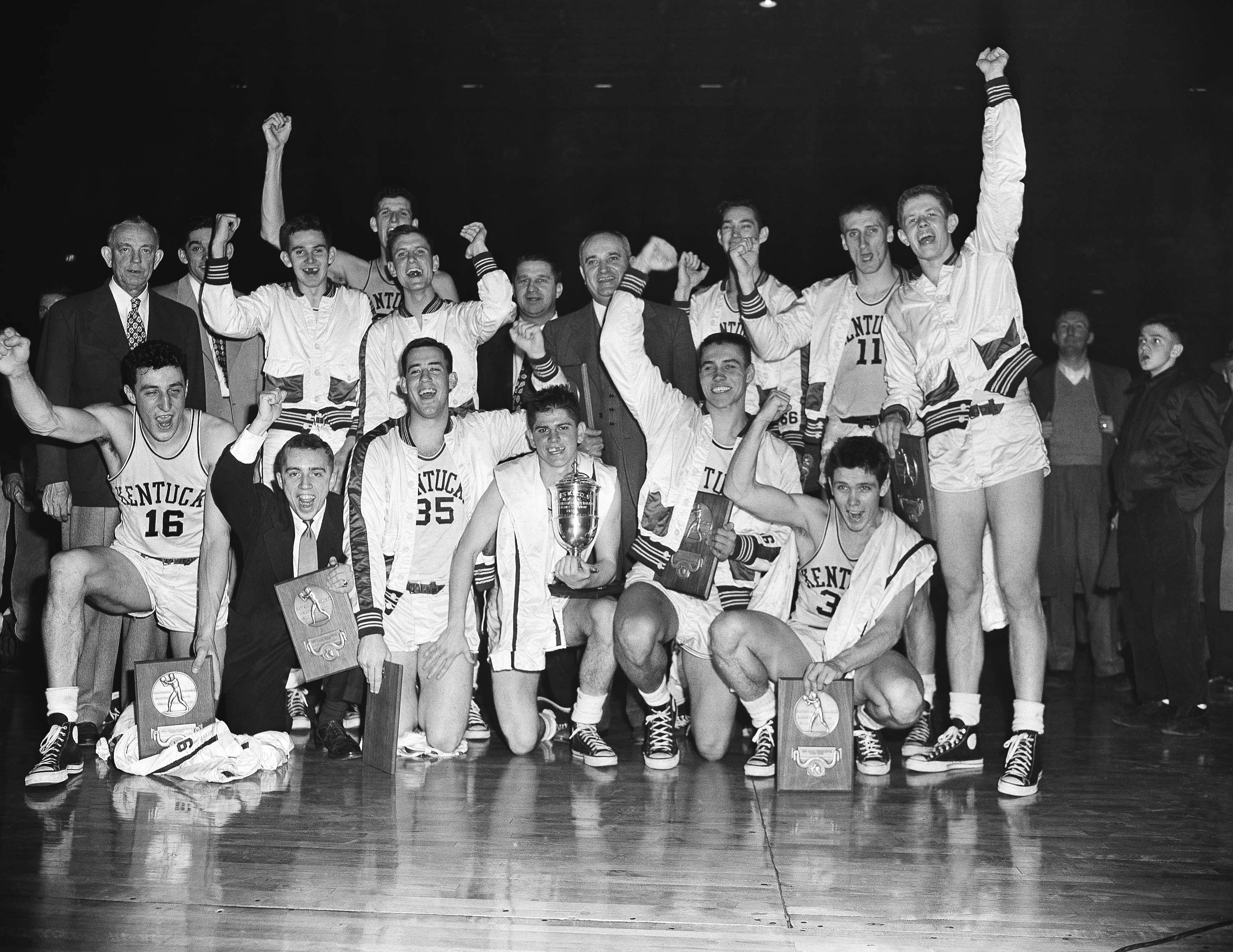 FILE - The Kentucky basketball team, which won the 1951 NCAA basketball championship, celebrates in Minneapolis, March 28, 1951, as it displays the team trophy and individual plaques. At center right is coach Adolph Rupp. Team members are, front row from left: Louis Tsioropoulos, C.M. Newton, Bobby Watson, Cliff Hagen, Lucian Whitaker and Frank Ramsey. Rear, from left: Dwight Price, Bill Spivey, Guy Strong, Roger Layne and Shelby Linville. 