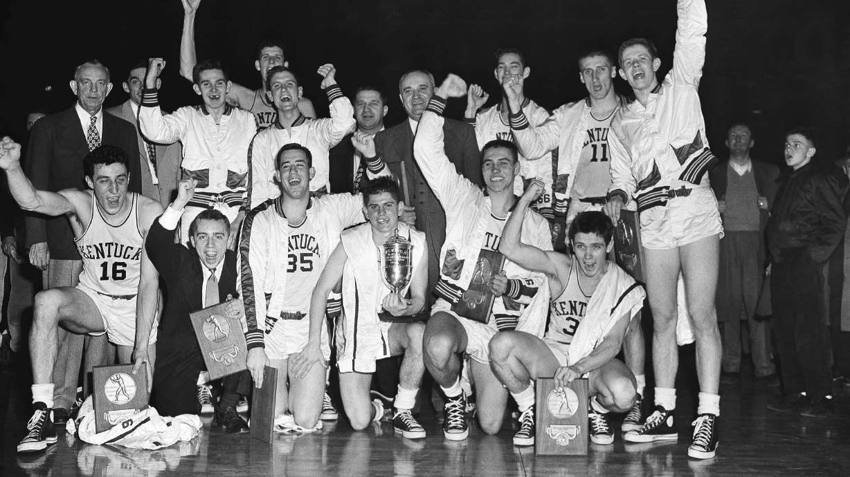 FILE - The Kentucky basketball team, which won the 1951 NCAA basketball championship, celebrates in Minneapolis, March 28, 1951, as it displays the team trophy and individual plaques. At center right is coach Adolph Rupp. Team members are, front row from left: Louis Tsioropoulos, C.M. Newton, Bobby Watson, Cliff Hagen, Lucian Whitaker and Frank Ramsey. Rear, from left: Dwight Price, Bill Spivey, Guy Strong, Roger Layne and Shelby Linville.