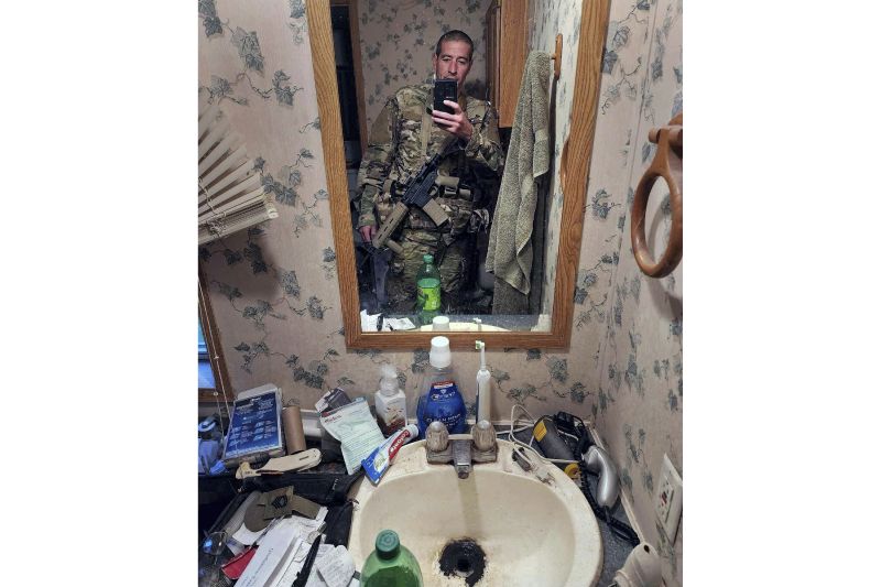 In this undated photo by Robert Card provided by Sean Hodgson, Card wears a camouflage uniform with a rifle slung across his chest.