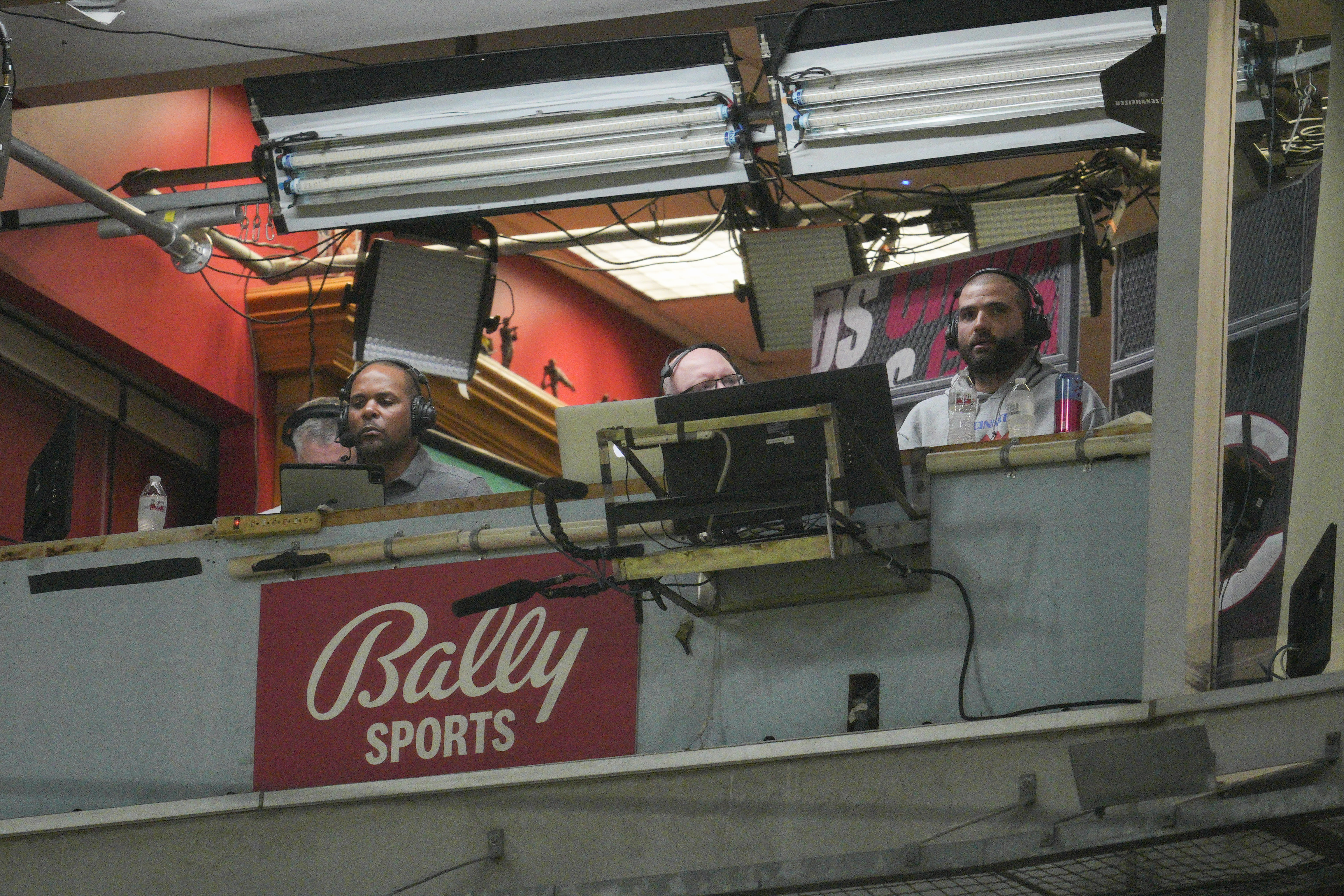 FILE - Cincinnati Reds' Joey Votto, right, sits in the broadcast booth with John Sadak, center right, and Barry Larkin, center left, during a baseball game against the St. Louis Cardinals Wednesday, Aug. 31, 2022, in Cincinnati. Amazon will partner with the Diamond Sports as part of a restructuring agreement as the largest owner of regional sports networks looks to emerge from bankruptcy. Diamond owns 18 networks under the Bally Sports banner. Those networks have the rights to 37 professional teams — 11 baseball, 15 NBA and 11 NHL.