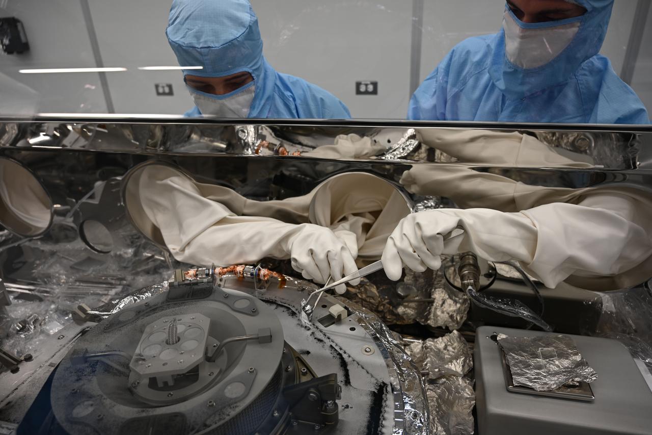 Mari Montoya, left, and Curtis Calva collect asteroid particles from the base of the OSIRIS-REx science canister.