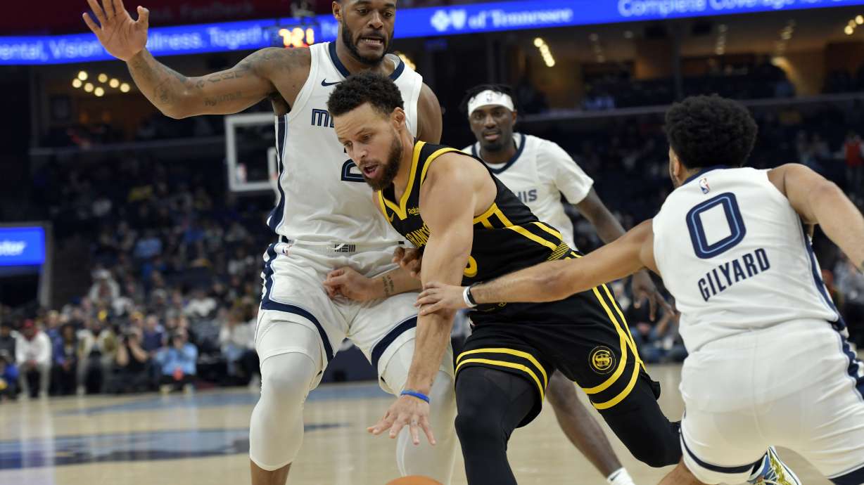 Golden State Warriors guard Stephen Curry, center, drives between Memphis Grizzlies forward Xavier Tillman (2) and guard Jacob Gilyard (0) in the first half of an NBA basketball game Monday, Jan. 15, 2024, in Memphis, Tenn.