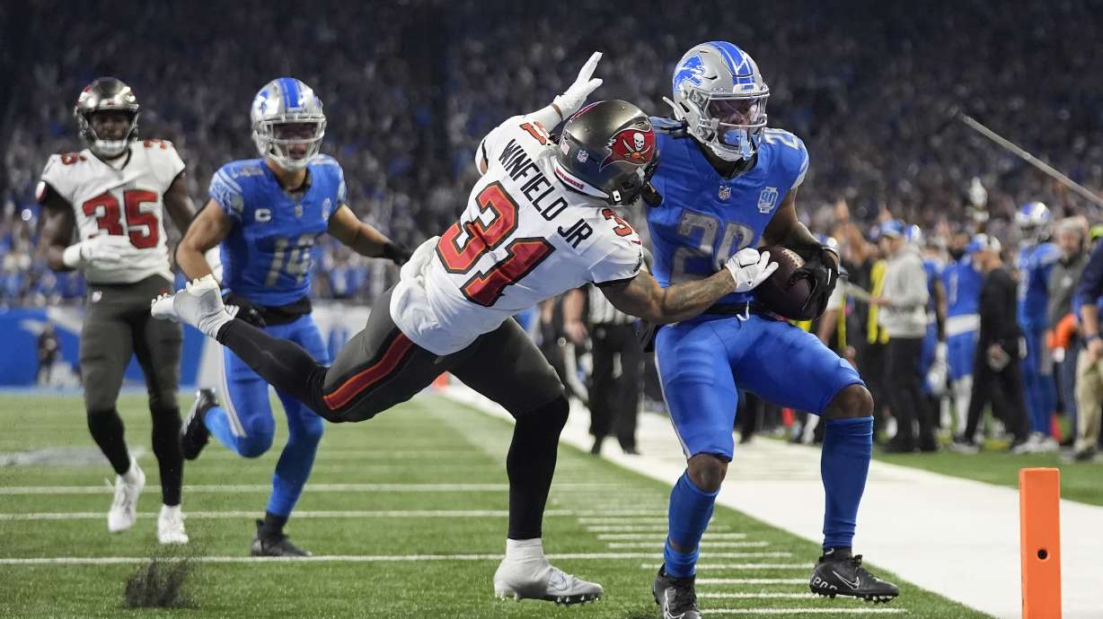 Detroit Lions running back Jahmyr Gibbs, right, avoids a hit by Tampa Bay Buccaneers safety Antoine Winfield Jr. (31) while scoring on a touchdown run during the second half of an NFL football NFC divisional playoff game, Sunday, Jan. 21, 2024, in Detroit. Buccaneers' Jamel Dean (35) and Lions' Amon-Ra St. Brown (14) look on.