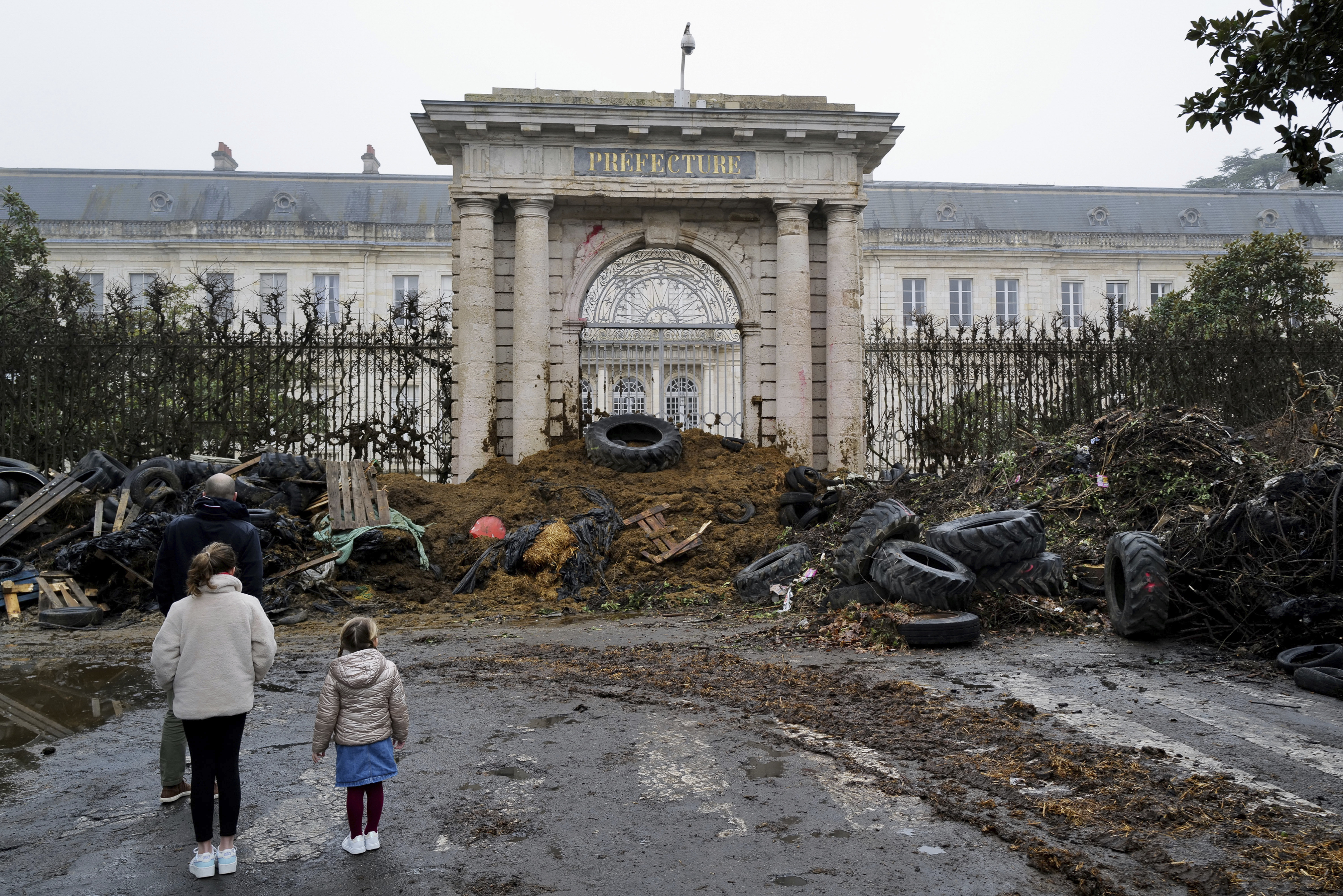 People watch slurry, manure and tires dumped by farmers at the entrance of the local state administration building in Agen, southwestern France, Saturday. French farmers have vowed to continue protesting and are maintaining traffic barricades on some of the country's major roads. 