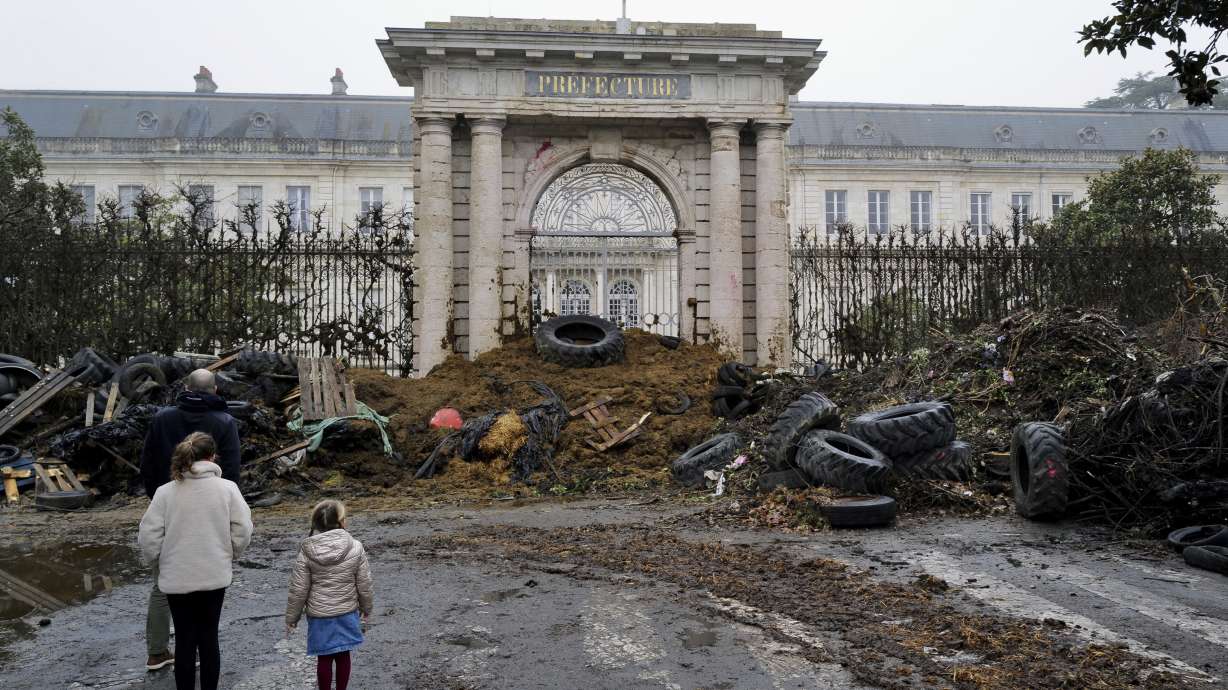 People watch slurry, manure and tires dumped by farmers at the entrance of the local state administration building in Agen, southwestern France, Saturday. French farmers have vowed to continue protesting and are maintaining traffic barricades on some of the country's major roads.