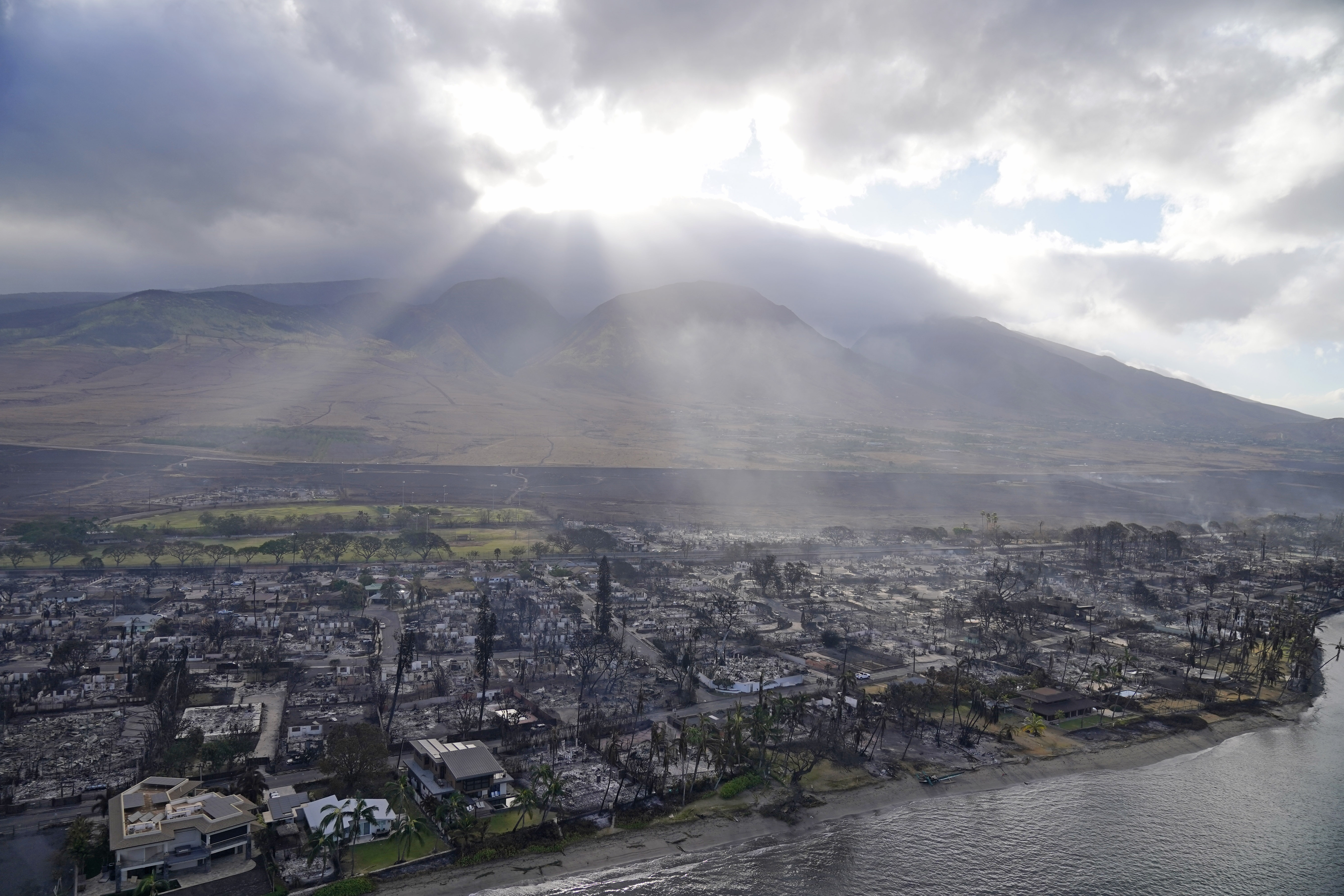 Rays of sunlight pierce through the clouds, Aug. 10, 2023, above homes burned by wildfires in Lahaina, Hawaii. Better communications and equipment are among the recommendations being made by the Maui Police Department in a report released Tuesday.