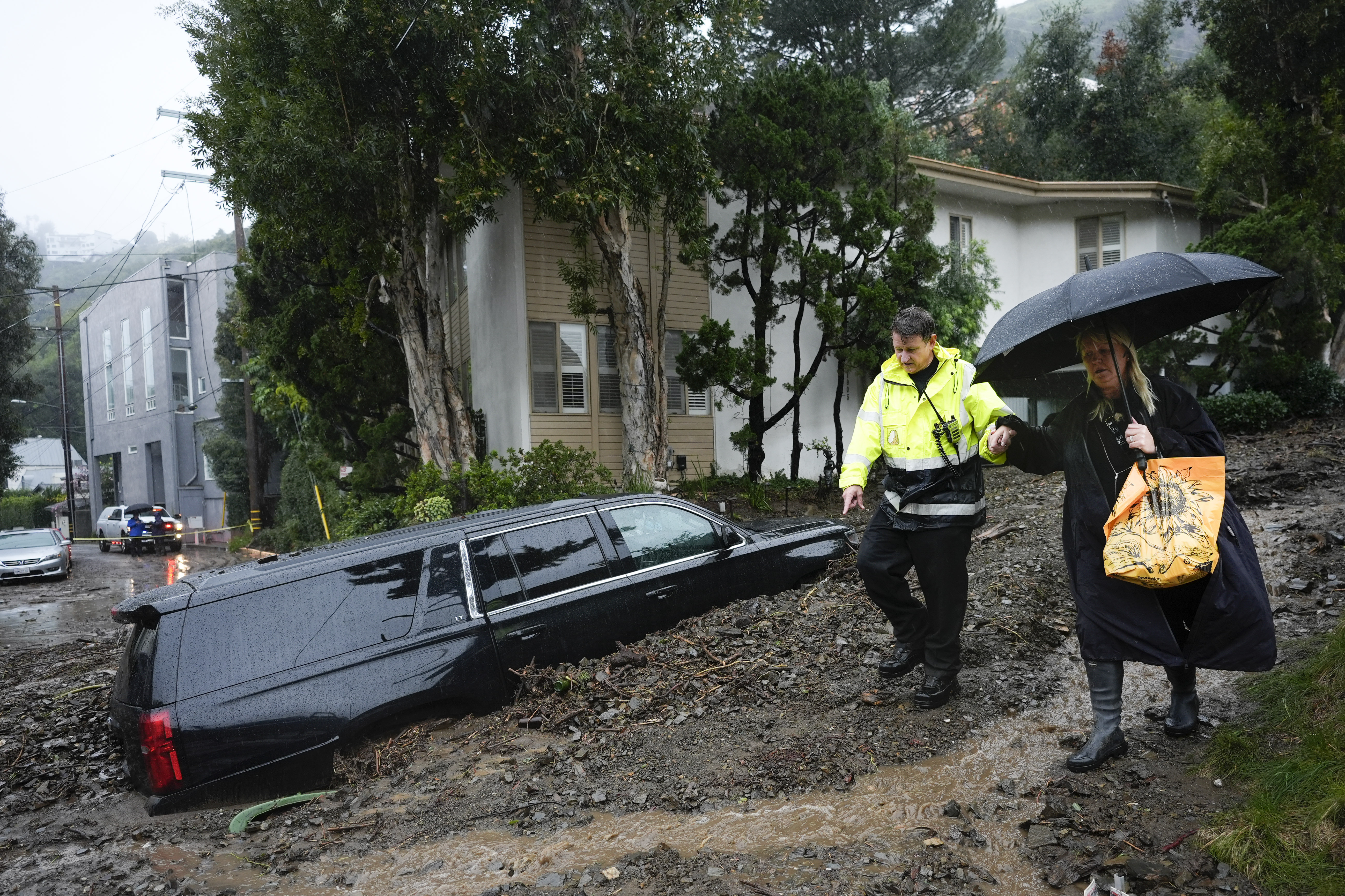 A first responder helps a resident evacuate from a neighborhood after a mudslide, Monday, in the Beverly Crest area of Los Angeles. A storm of historic proportions unleashed record levels of rain over parts of Los Angeles on Monday.