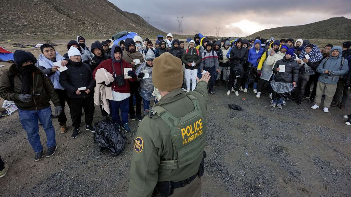 A Border Patrol agent asks asylum-seeking migrants to line up in a makeshift, mountainous campsite after the group crossed the border with Mexico, Friday, near Jacumba Hot Springs, Calif.