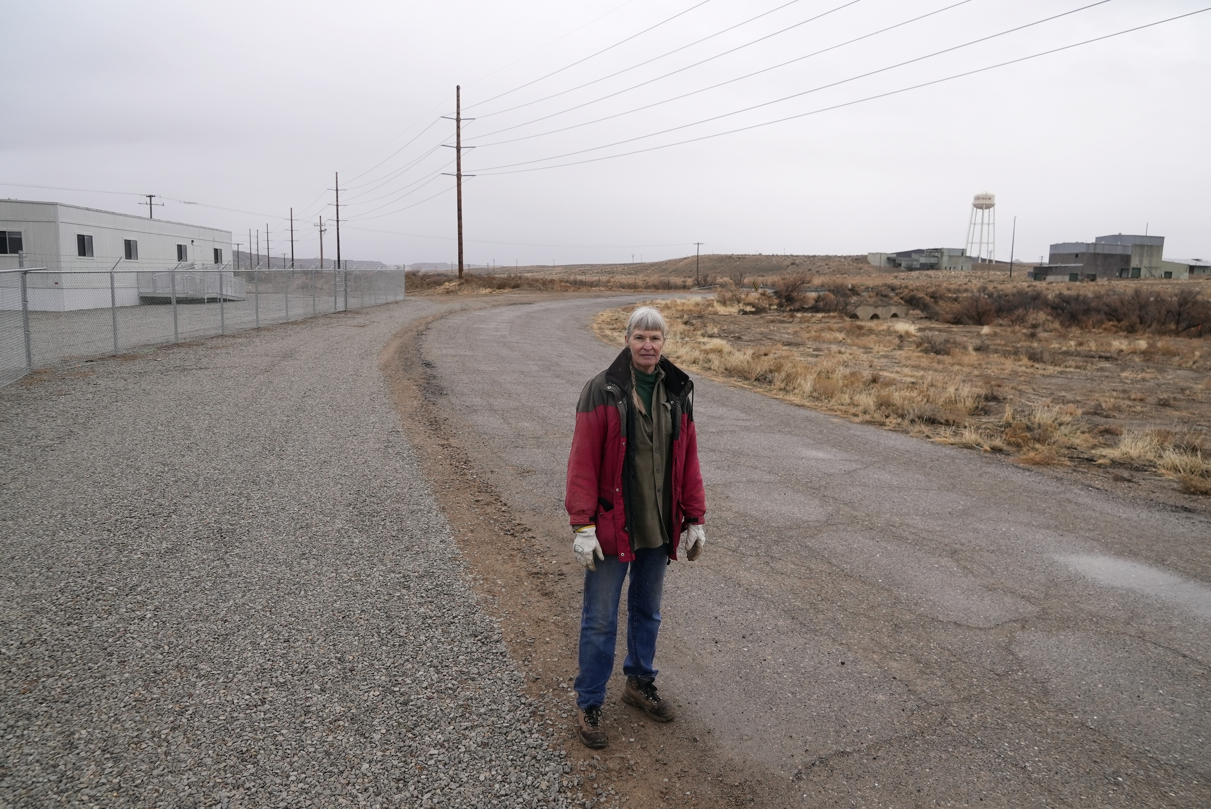 Gayna Salinas stands near a trailer, left, on land owned by Anson Resources, and a defunct uranium mine, right, Jan. 25, 2024, in Green River, Utah. The Australian company with its U.S. subsidiaries is eyeing a nearby area to extract lithium. Salinas, whose family farms in the rural community, said she was skeptical about the project's benefits.