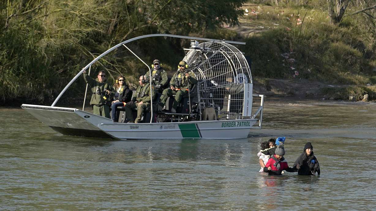 Border patrol agents watch as migrants cross the Rio Grande at the Texas-Mexico border, Jan. 3, in Eagle Pass, Texas.