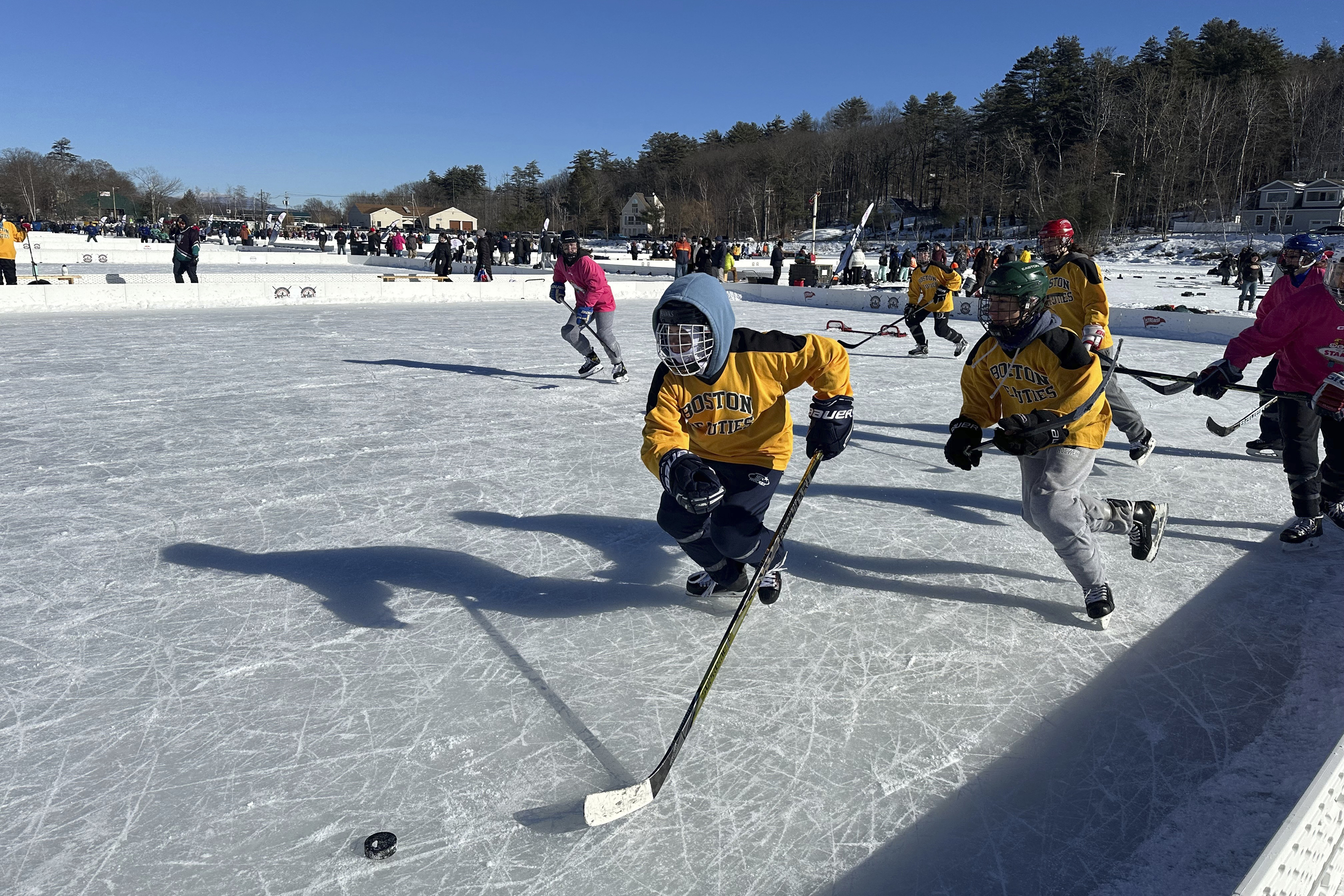 Hockey players go for the puck during the final of the women's open division at the Pond Hockey Classic in Meredith, N.H., on Sunday, Feb. 4, 2024. Like many winter traditions on lakes across the U.S., pond hockey is under threat from climate change. 