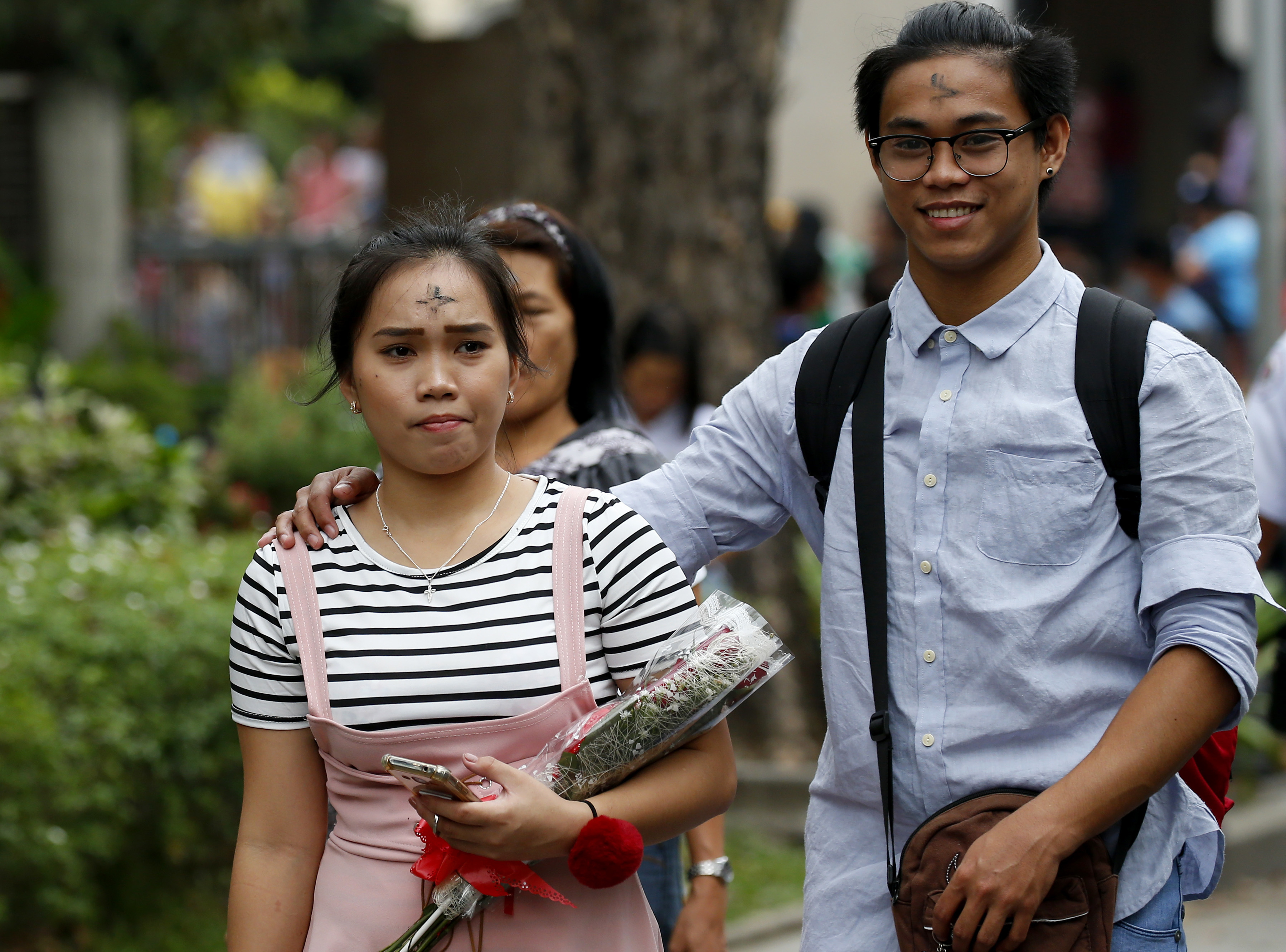 With their foreheads rubbed with ash in observance of Ash Wednesday, a couple emerges from a Catholic church with a bouquet of flowers on Valentine's day Wednesday, Feb. 14, 2018, in suburban Paranaque southeast of Manila, Philippines.