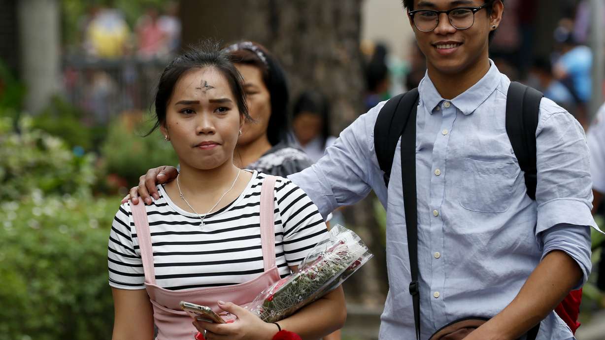 With their foreheads rubbed with ash in observance of Ash Wednesday, a couple emerges from a Catholic church with a bouquet of flowers on Valentine's day Wednesday, Feb. 14, 2018, in suburban Paranaque southeast of Manila, Philippines.