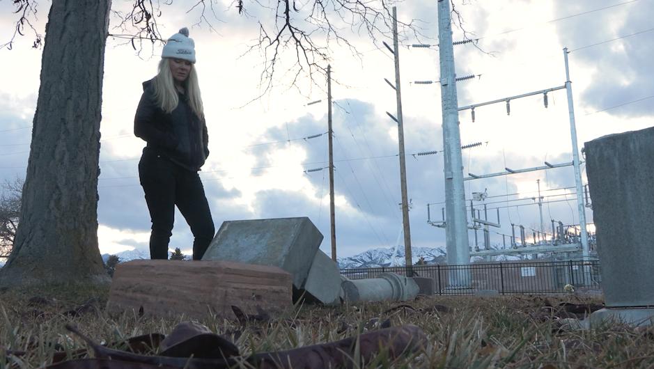 Susan Orifici stands over a broken headstone dating back to the late 1800s in Grantsville on Thursday.
