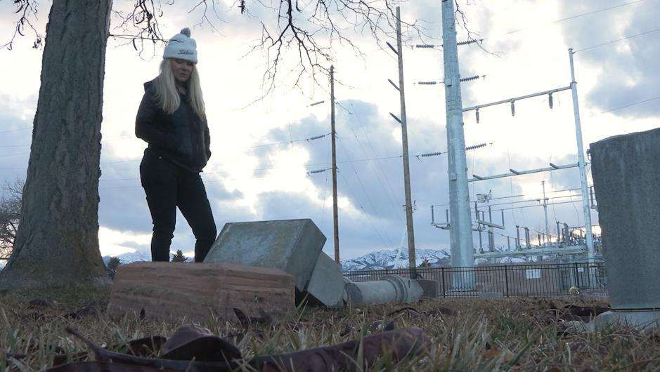 Susan Orifici stands over a broken headstone dating back to the late 1800s in Grantsville on Thursday.