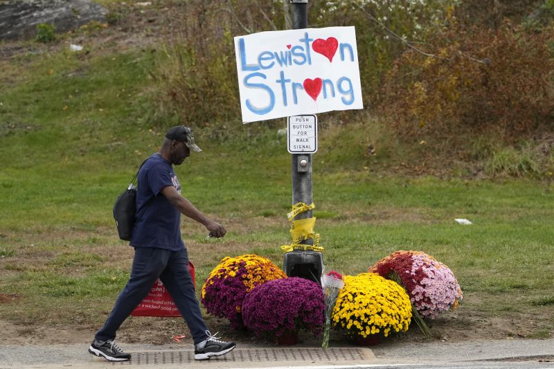 A man walks by flowers and a sign of support for the community, Oct. 28, 2023, in the wake of the mass shootings that occurred on Oct. 25, 2023, in Lewiston, Maine.