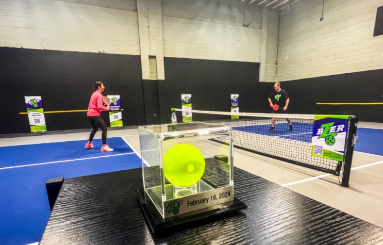 Pickleball pro and coach Callie Jo Smith, left, and former Utah congressman Ben McAdams, right, play pickleball in front of a miniature Bzer pickleball on display at Club Pickleball USA in Sandy on Friday.