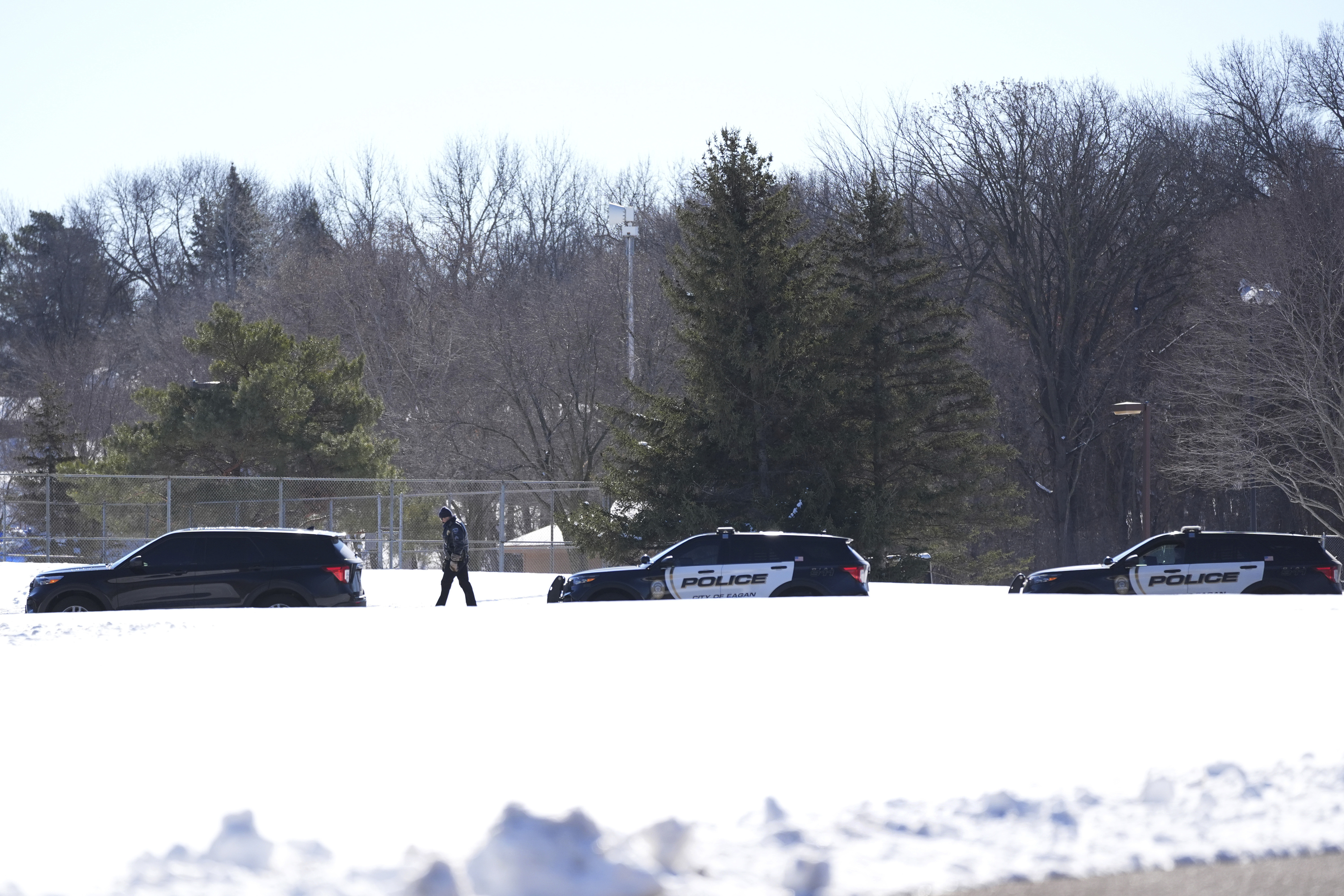 A police officer walks across a road after two police officers and a first responder were shot and killed Sunday in Burnsville, Minn.