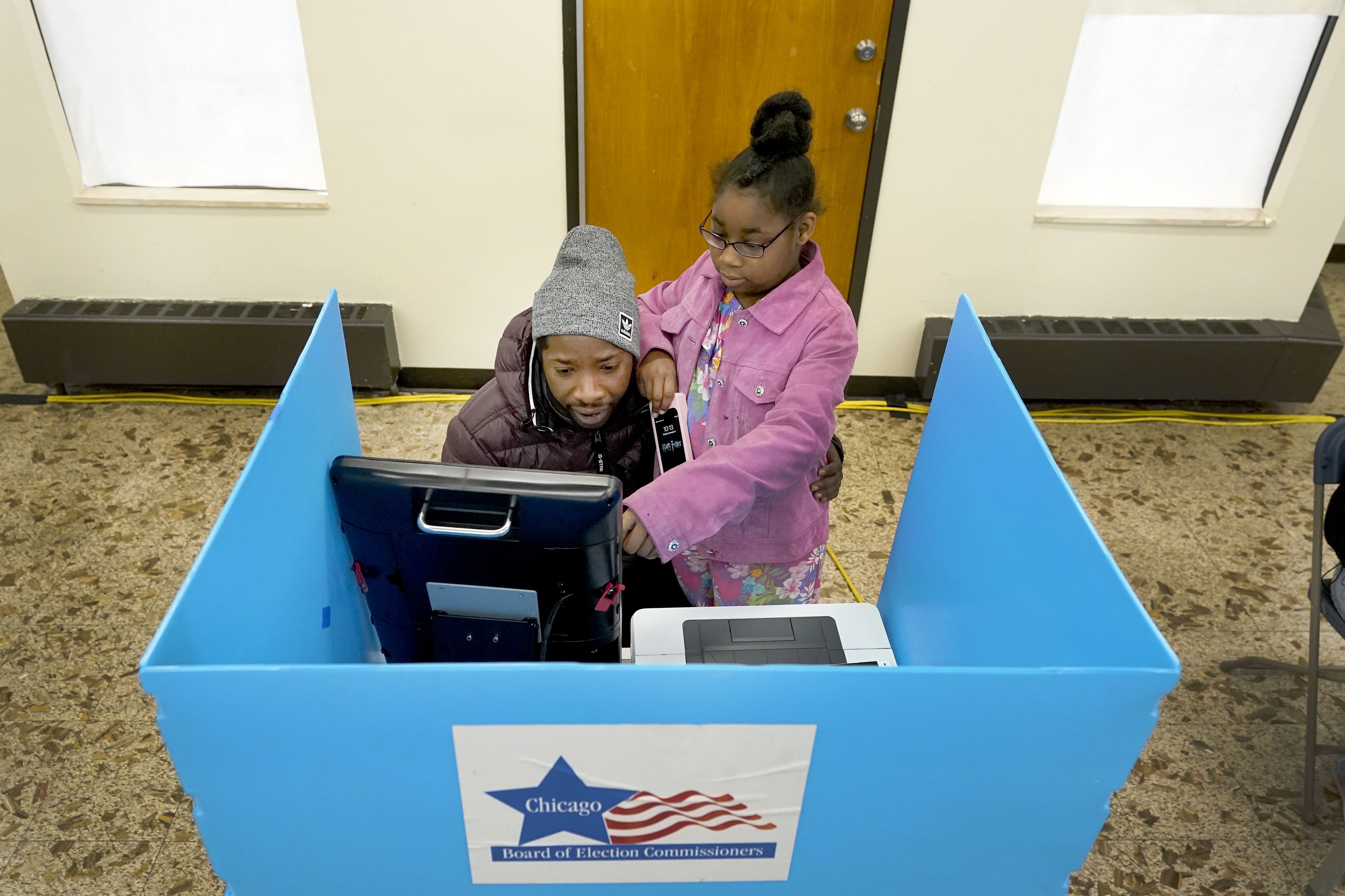 Christopher Sandridge teaches his daughter Christina the voting process as he casts a ballot at the Rev. Dr. Martin Luther King Community Center on the Southside of Chicago, Nov. 8, 2022. 