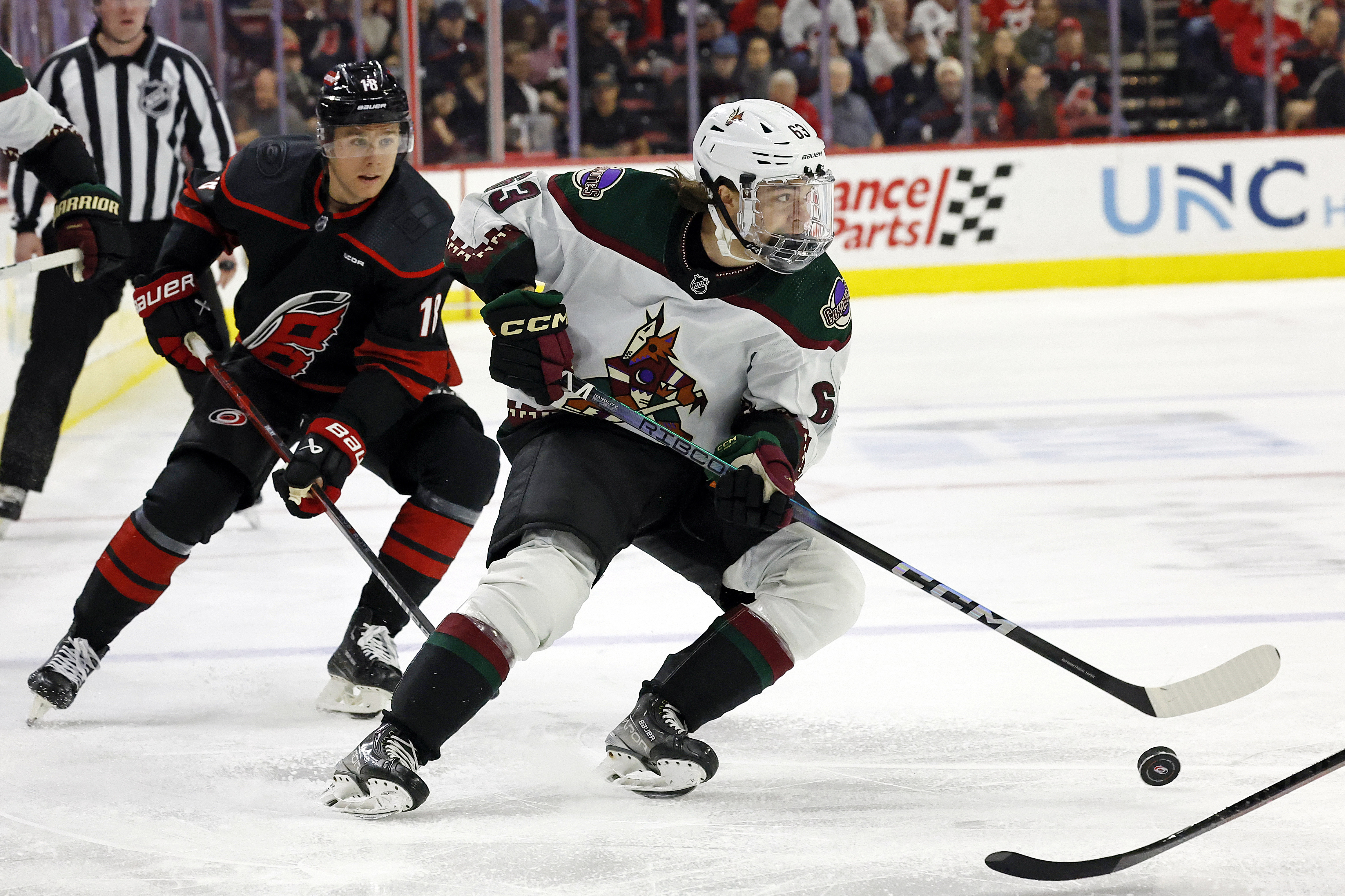Arizona Coyotes' Adam Ruzicka (63) controls the puck in front of Carolina Hurricanes' Jack Drury (18) during the first period of an NHL hockey game Saturday, Jan. 27, 2024, in Raleigh, N.C.