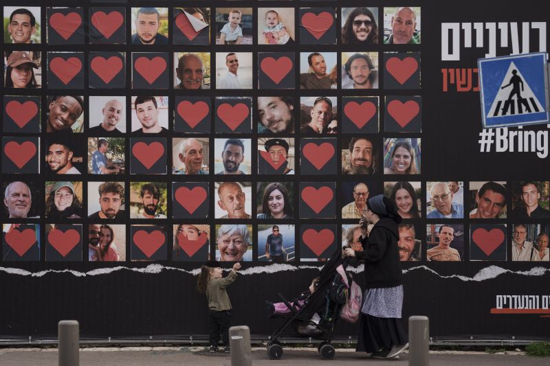 A woman and her children walk past a wall with photographs of hostages who were kidnapped during the Oct. 7 Hamas cross-border attack in Israel in Jerusalem, Israel, Monday.